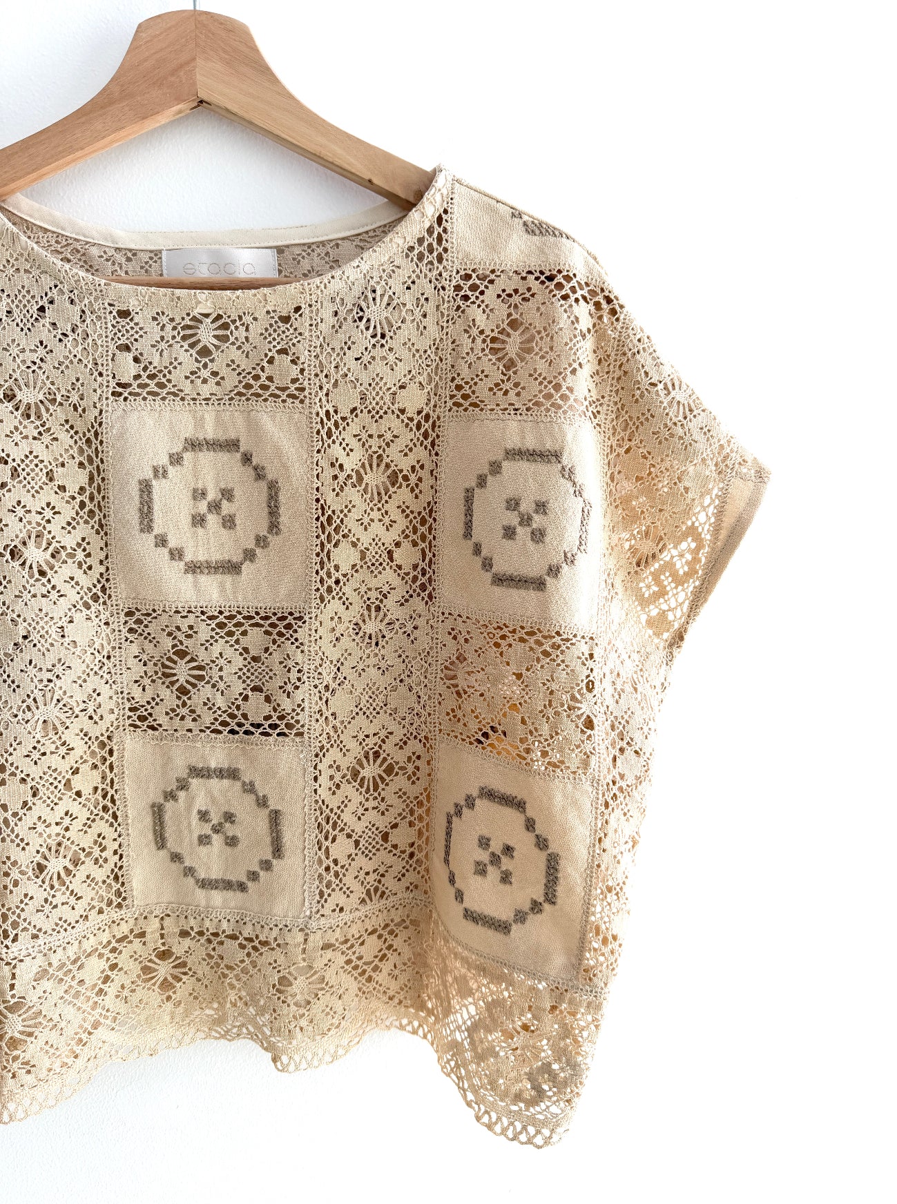Beige lace top with geometric patterns on a wooden hanger against a white background