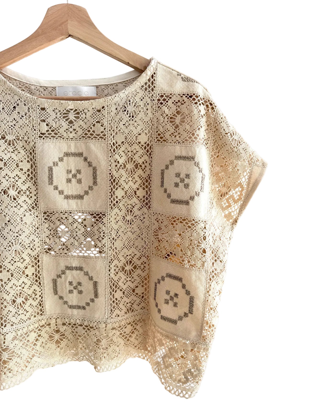 Beige lace top with geometric patterns on a wooden hanger against a white background