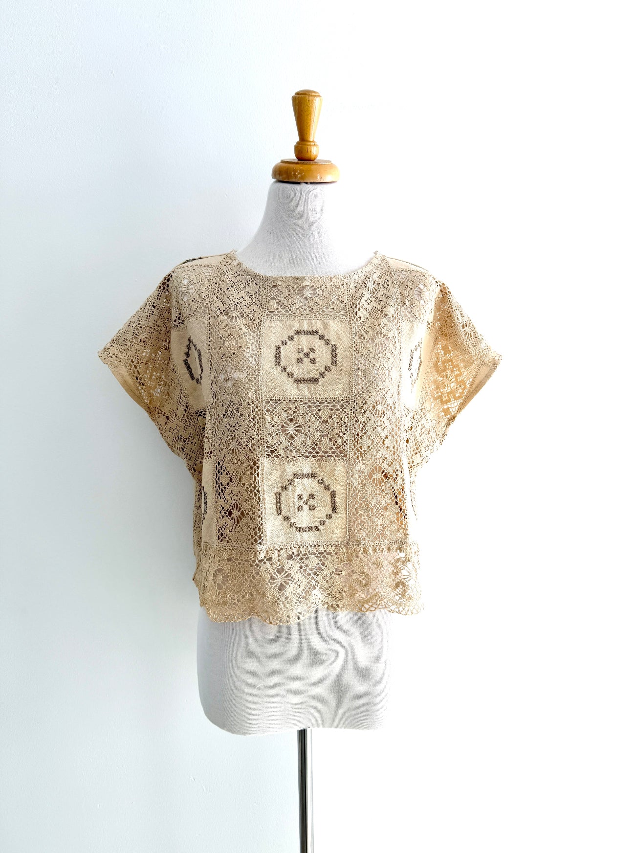 Beige crochet top on a mannequin against a white background