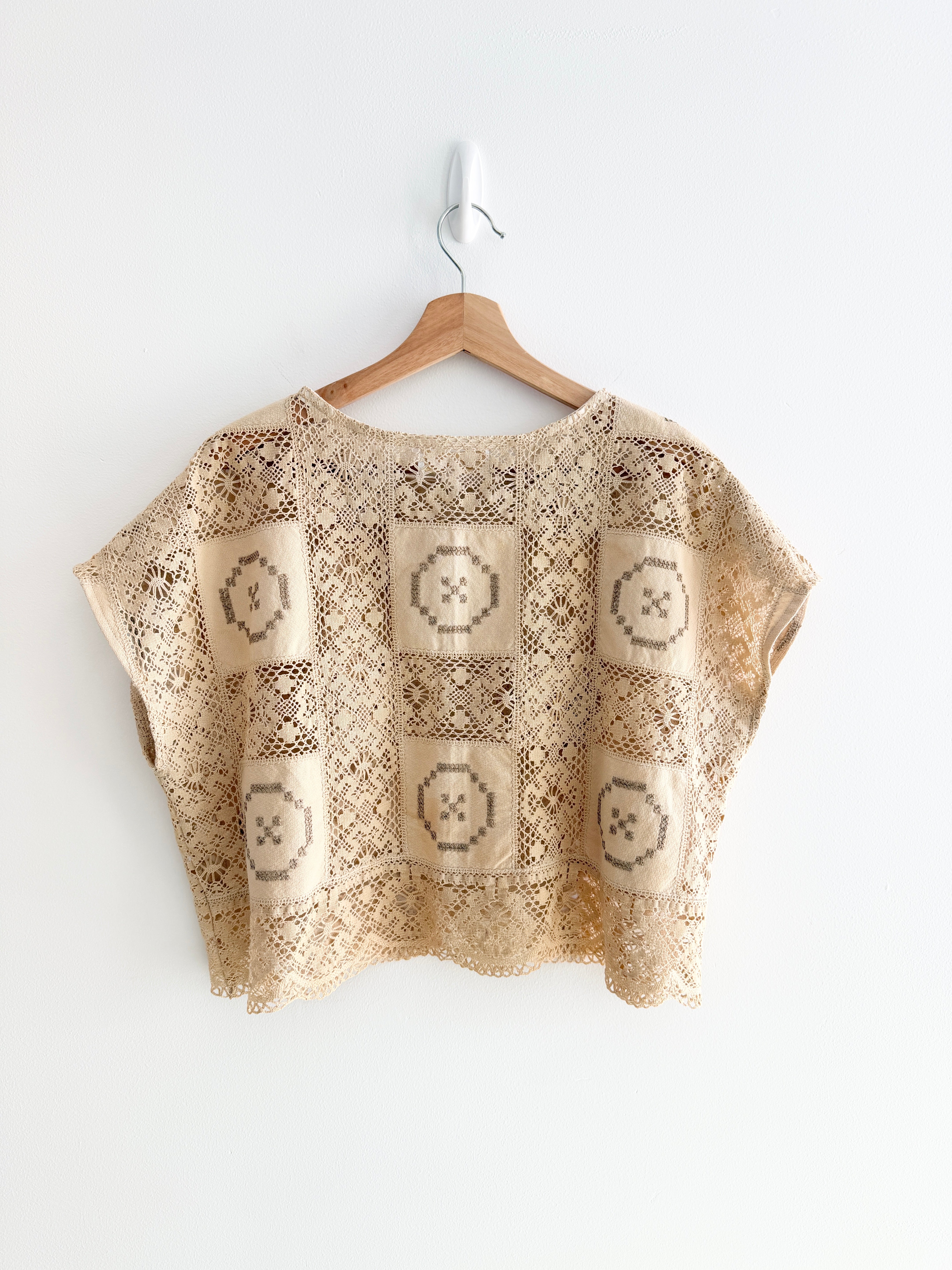 Beige crochet top with geometric pattern on a wooden hanger against a white background