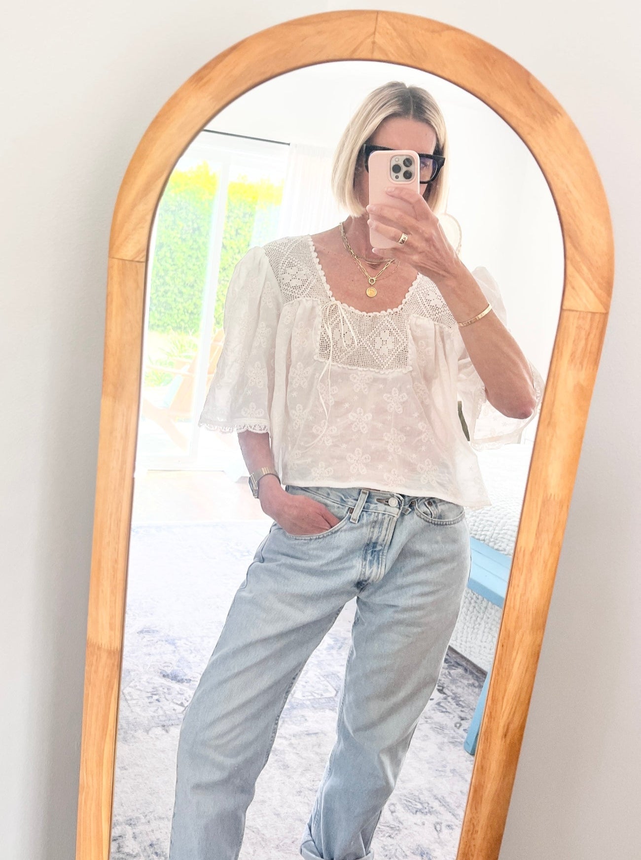 Person wearing a white blouse and light blue jeans standing in front of a long mirror with a wooden frame.