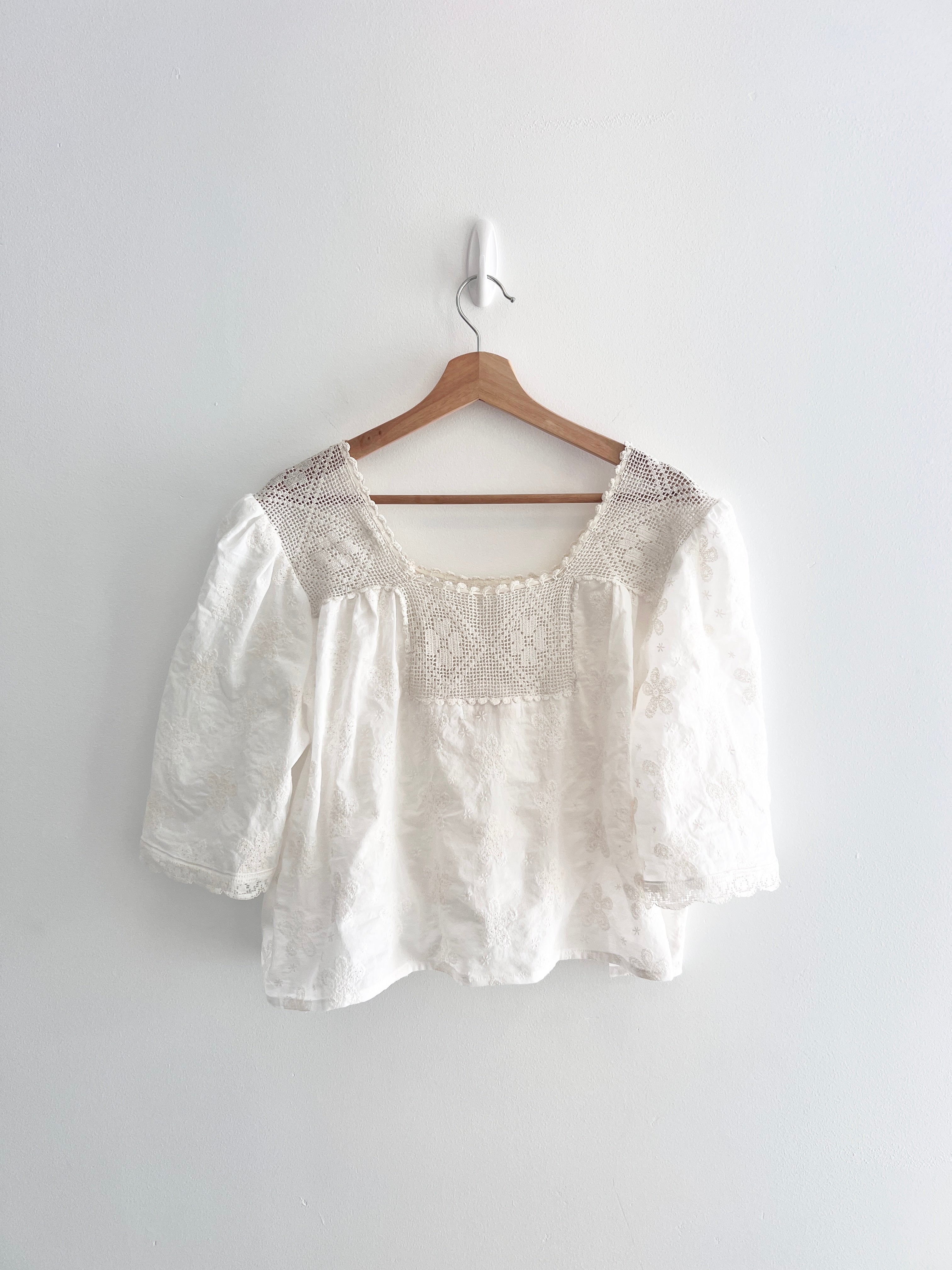 White blouse with lace details on a wooden hanger against a white background