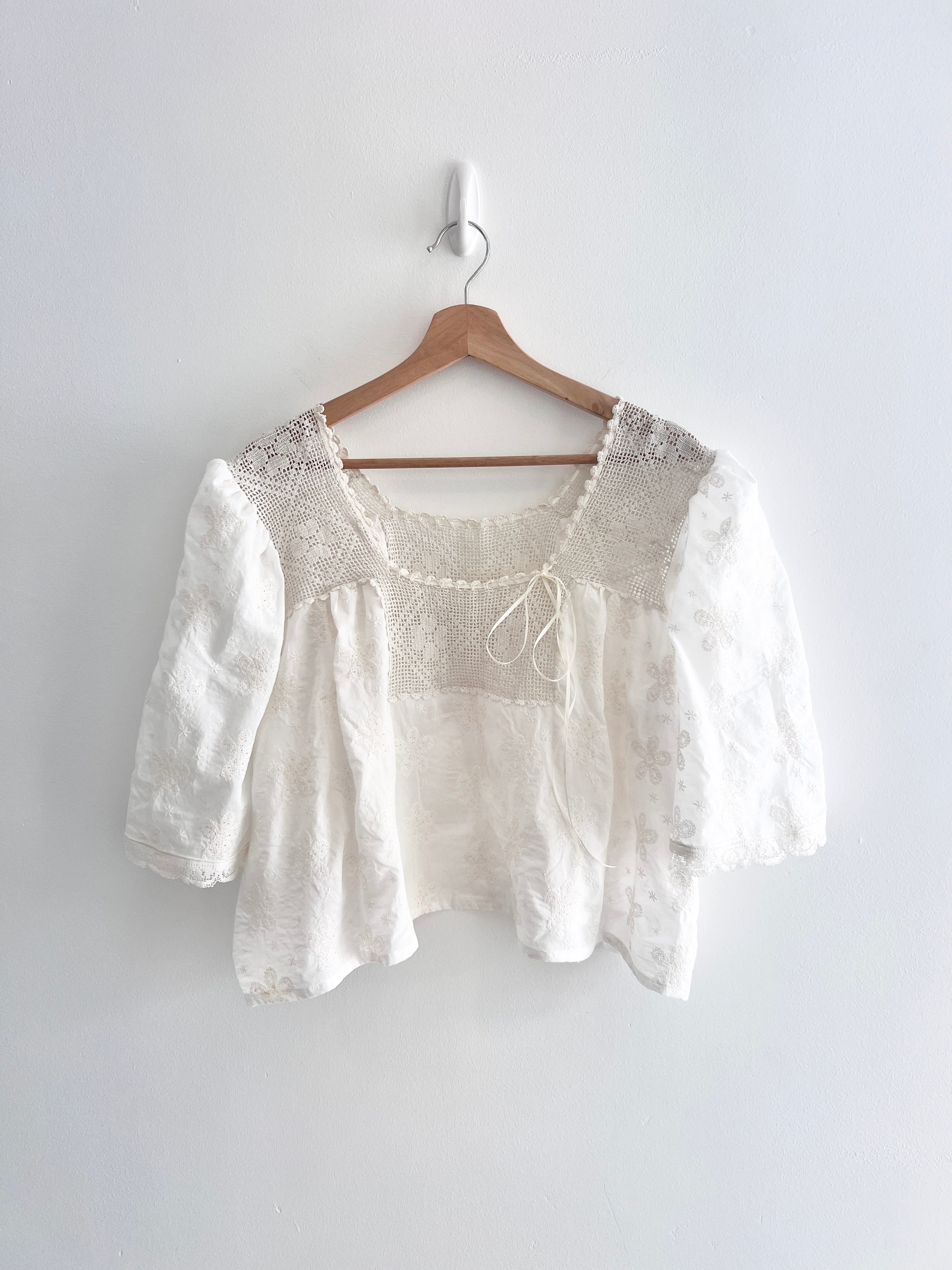 White blouse with lace details on a wooden hanger against a white wall
