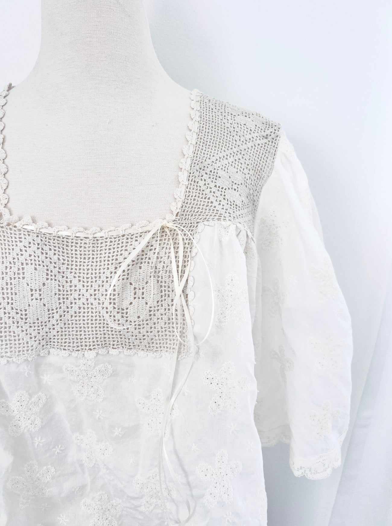 White blouse with intricate detailing on a mannequin against a white background