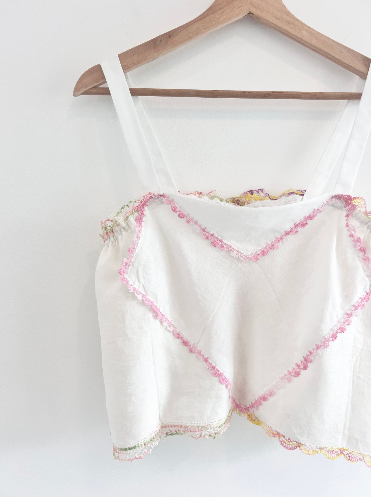 White tank top with pink floral trim on a wooden hanger against a white background