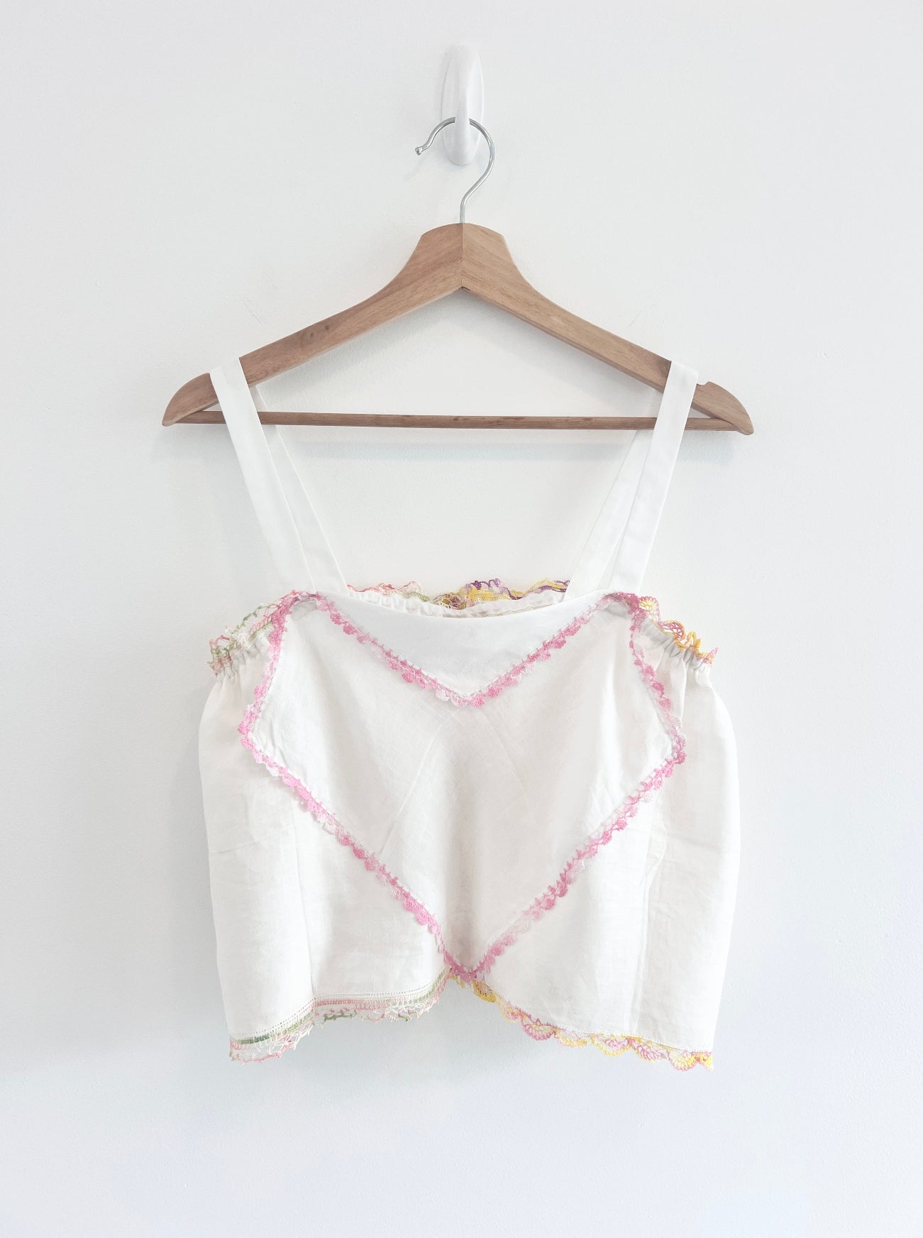 White tank top with pink and yellow pattern on a wooden hanger against a white background