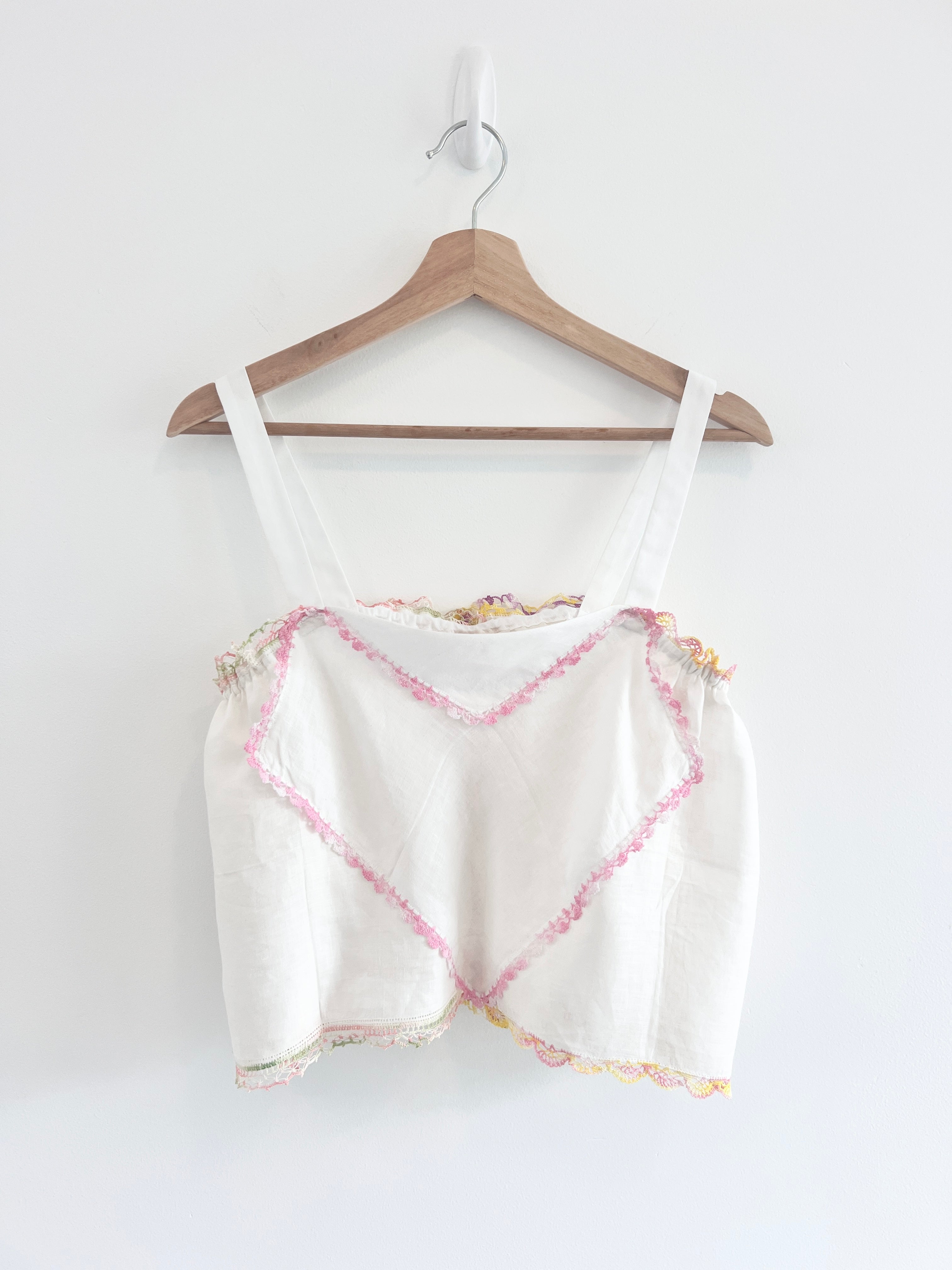White tank top with pink and yellow pattern on a wooden hanger against a white background