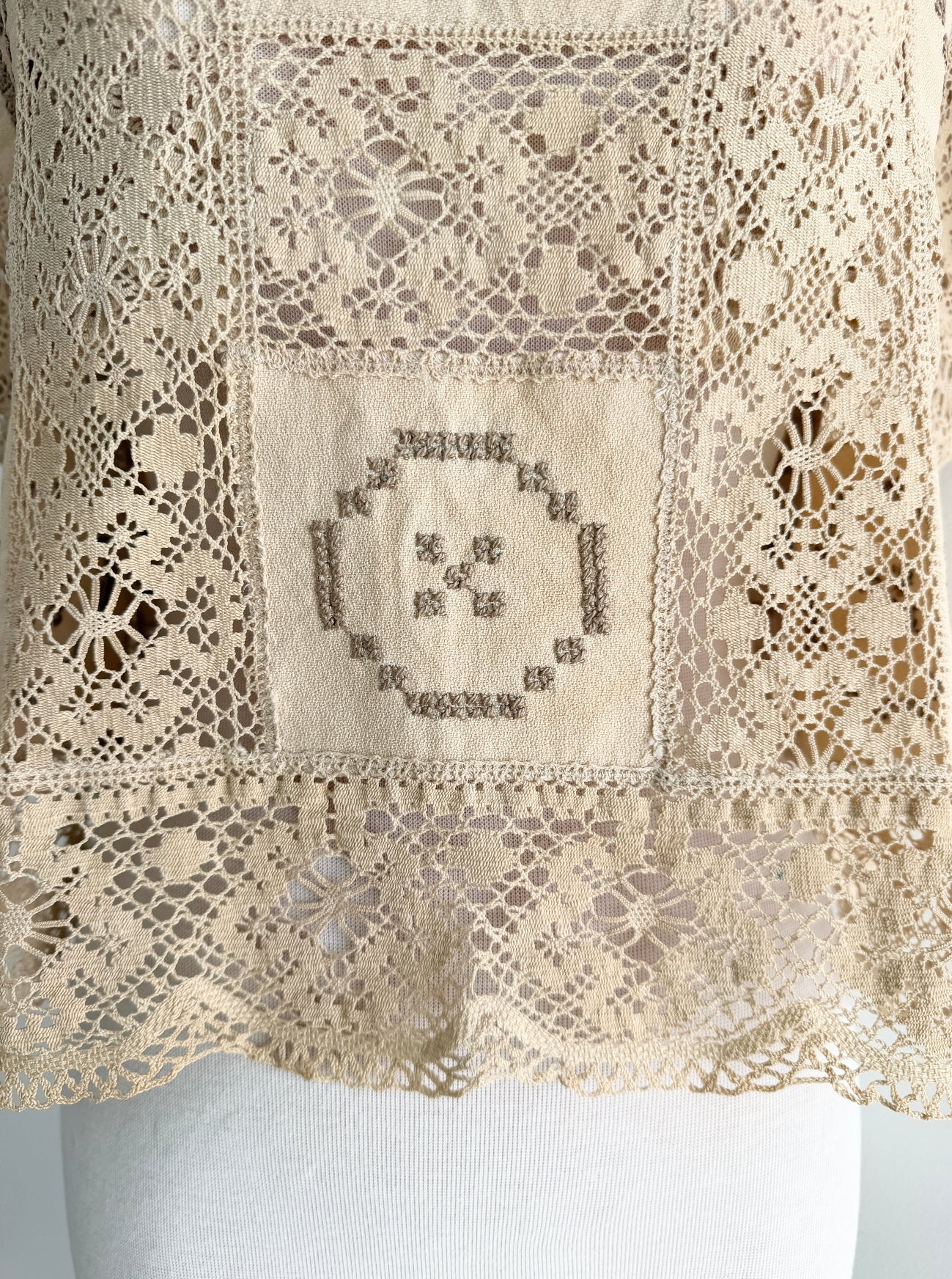 Close-up of a beige lace fabric with intricate patterns and a central embroidered design.