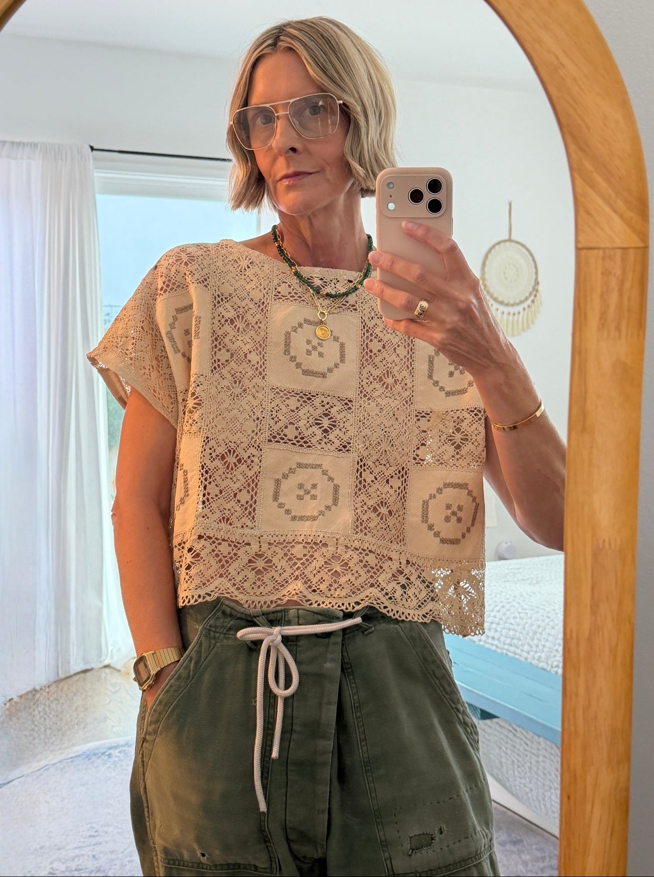 Person taking a mirror selfie wearing a patterned top and green pants indoors.
