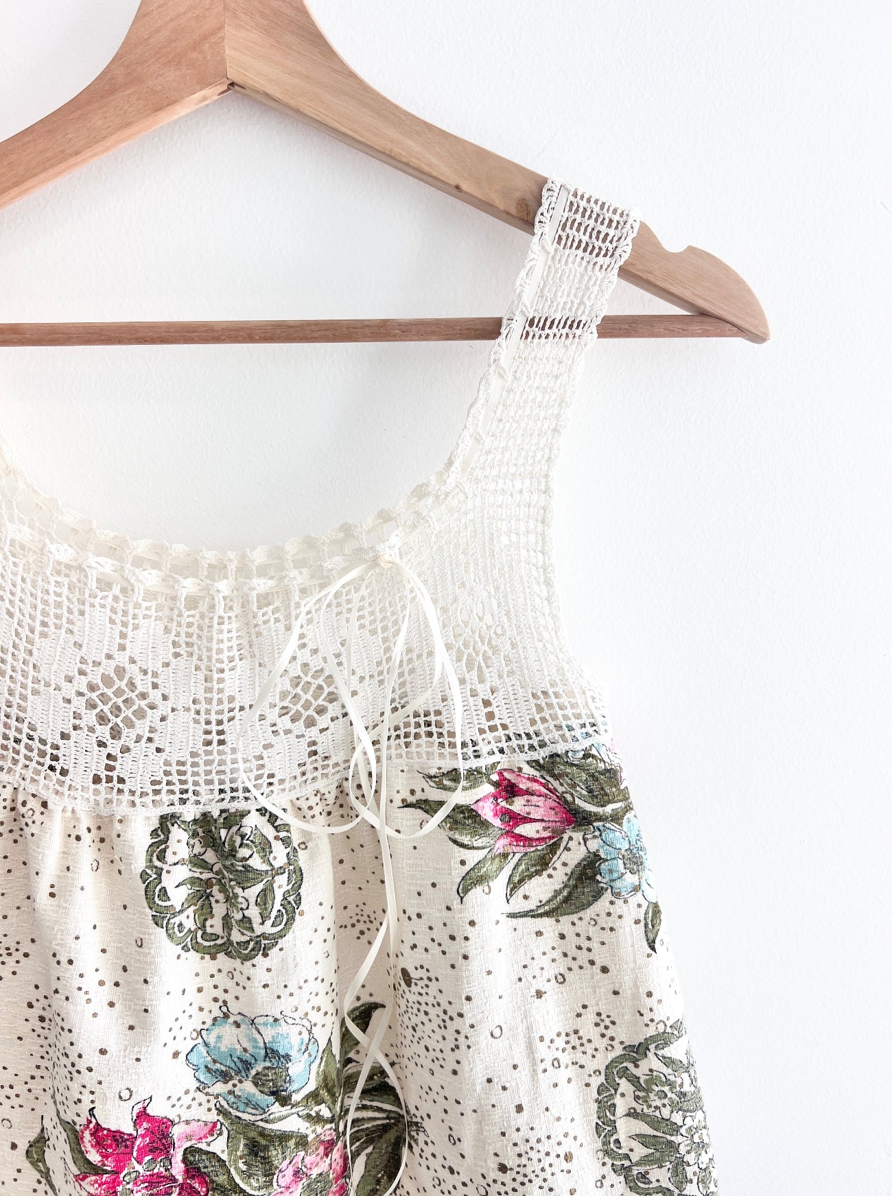 White lace top with floral embroidery on a wooden hanger against a white background