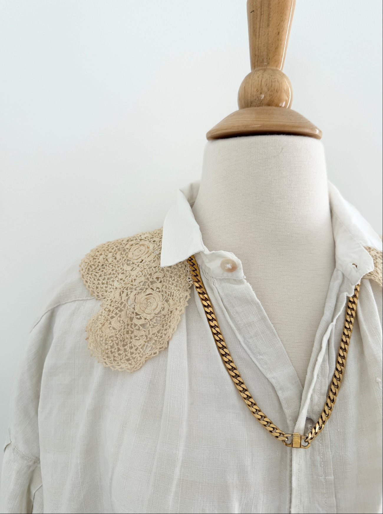 Mannequin wearing a white shirt with crochet details and a gold chain necklace on a plain background
