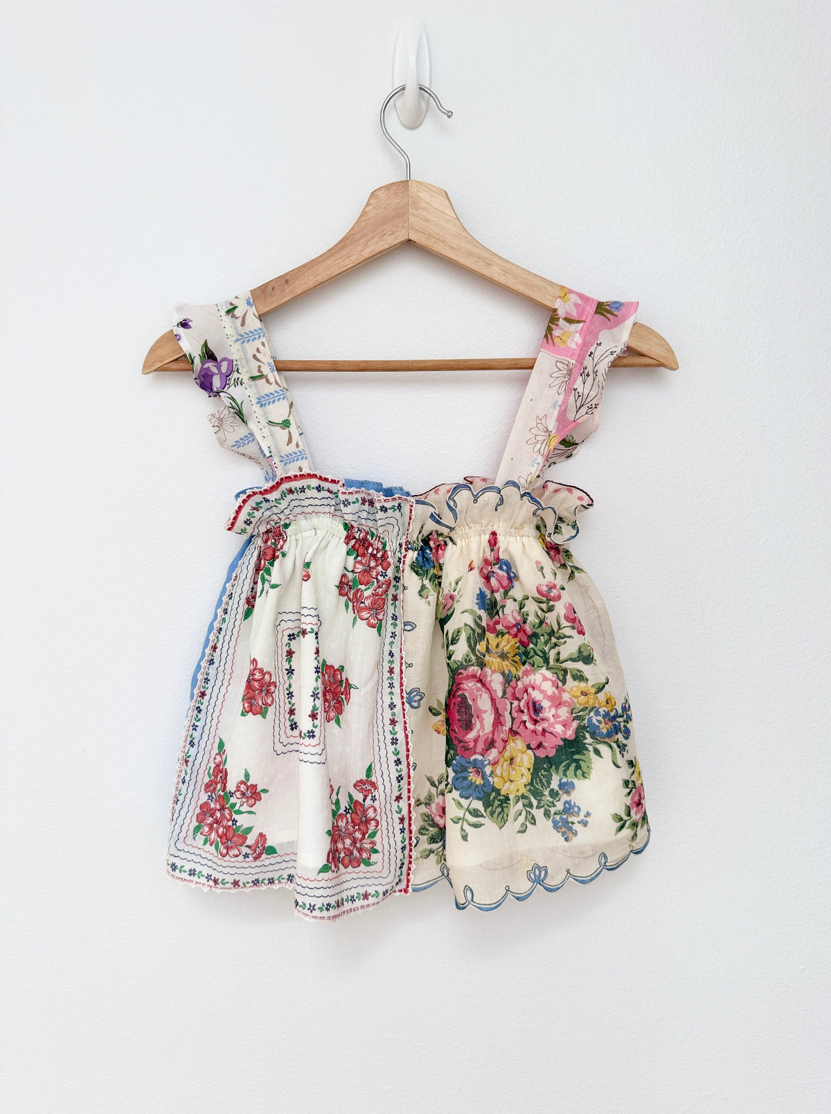 A sleeveless top with a split floral print design, hanging on a wooden hanger against a plain white wall.