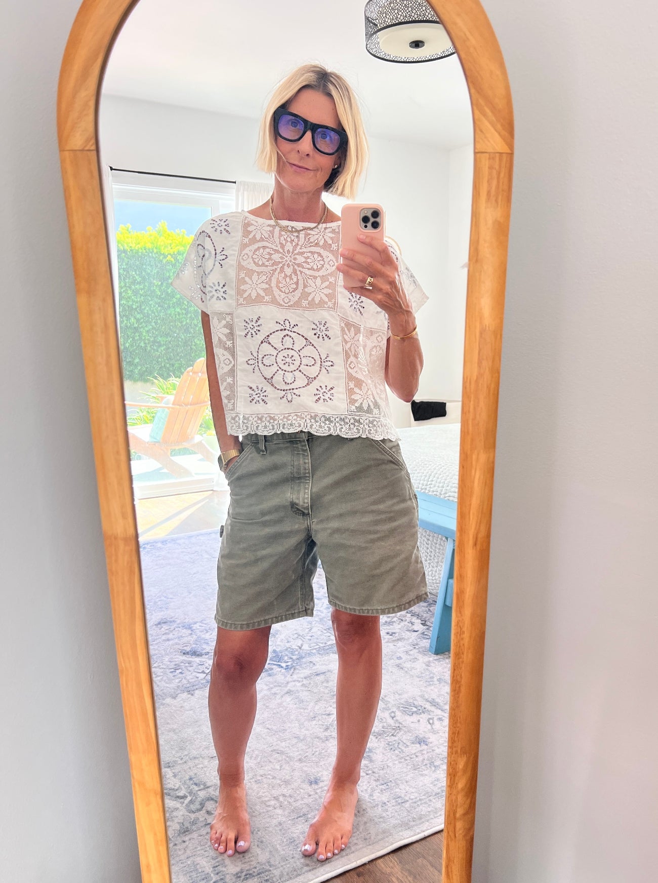 Person taking a mirror selfie wearing a white lace top and green shorts.
