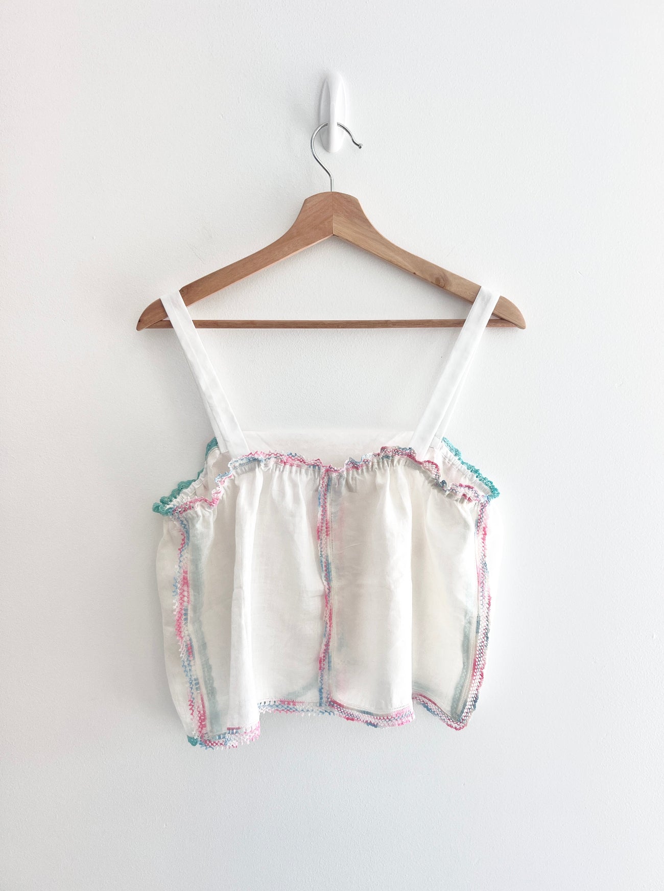 White top with colorful trim on a wooden hanger against a white background