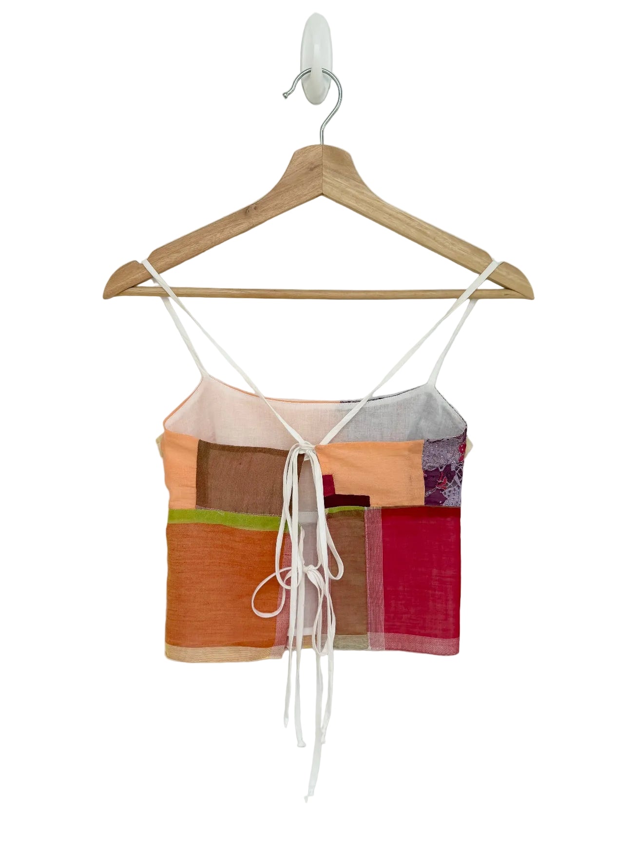 Colorful top with a patchwork design on a wooden hanger against a white background