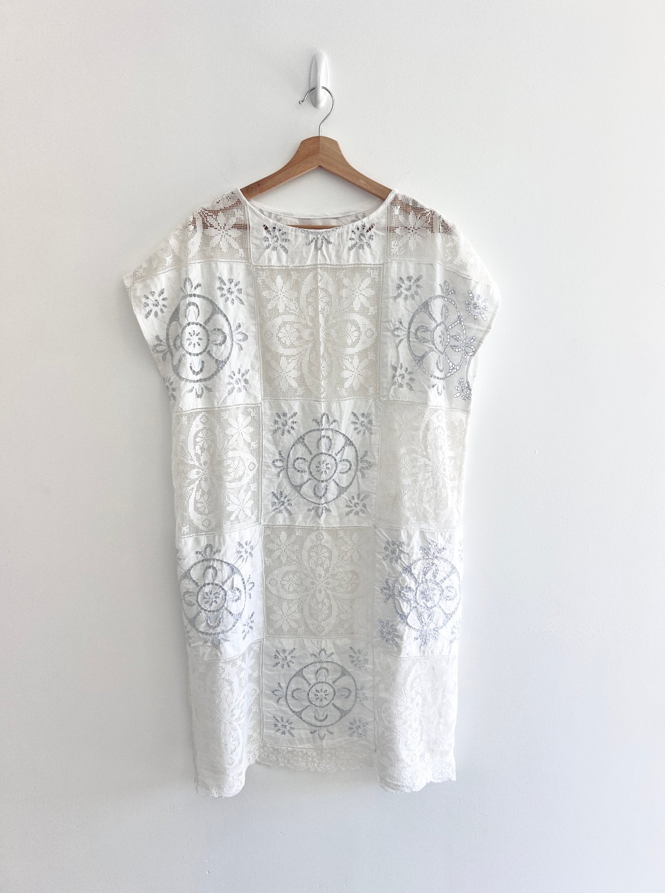 White dress with intricate patterns on a hanger against a white background