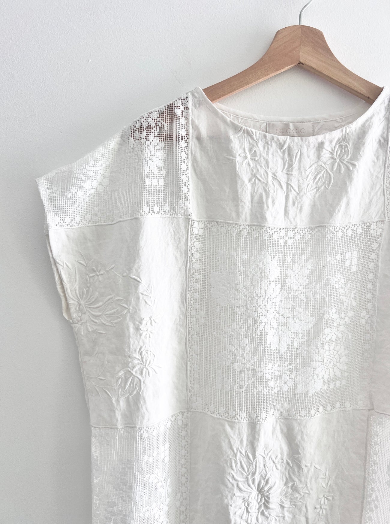White embroidered dress on a wooden hanger against a white background