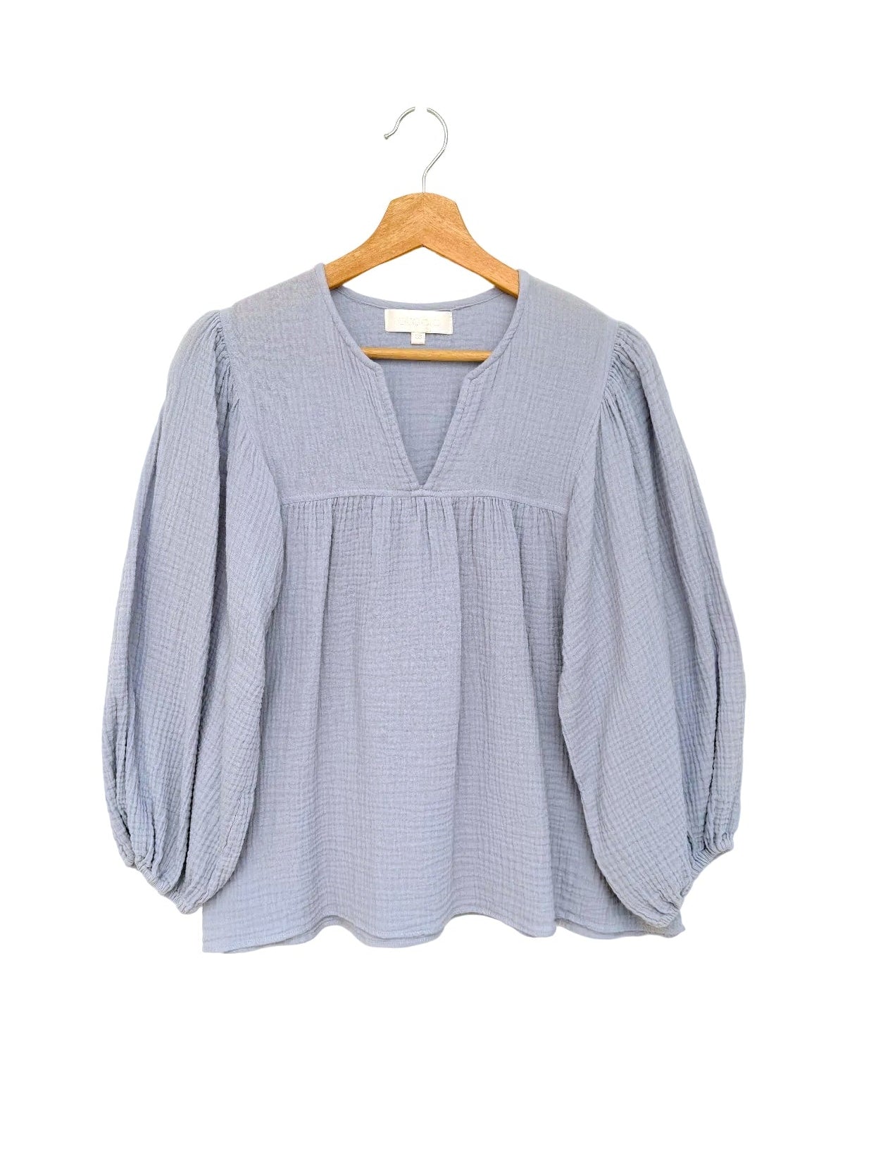 A light blue textured blouse with a V-neckline and voluminous balloon sleeves, hanging on a wooden hanger against a plain white background.