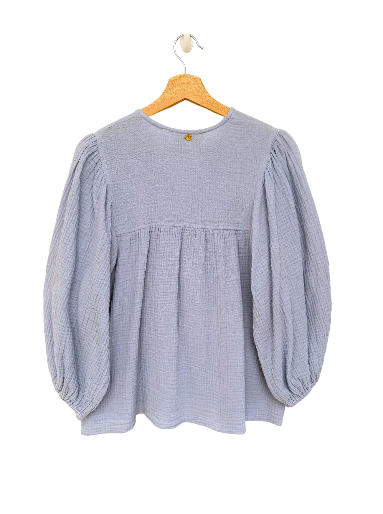 A light blue textured long-sleeve blouse with a gathered empire waist and balloon sleeves, hanging on a wooden hanger against a white background.