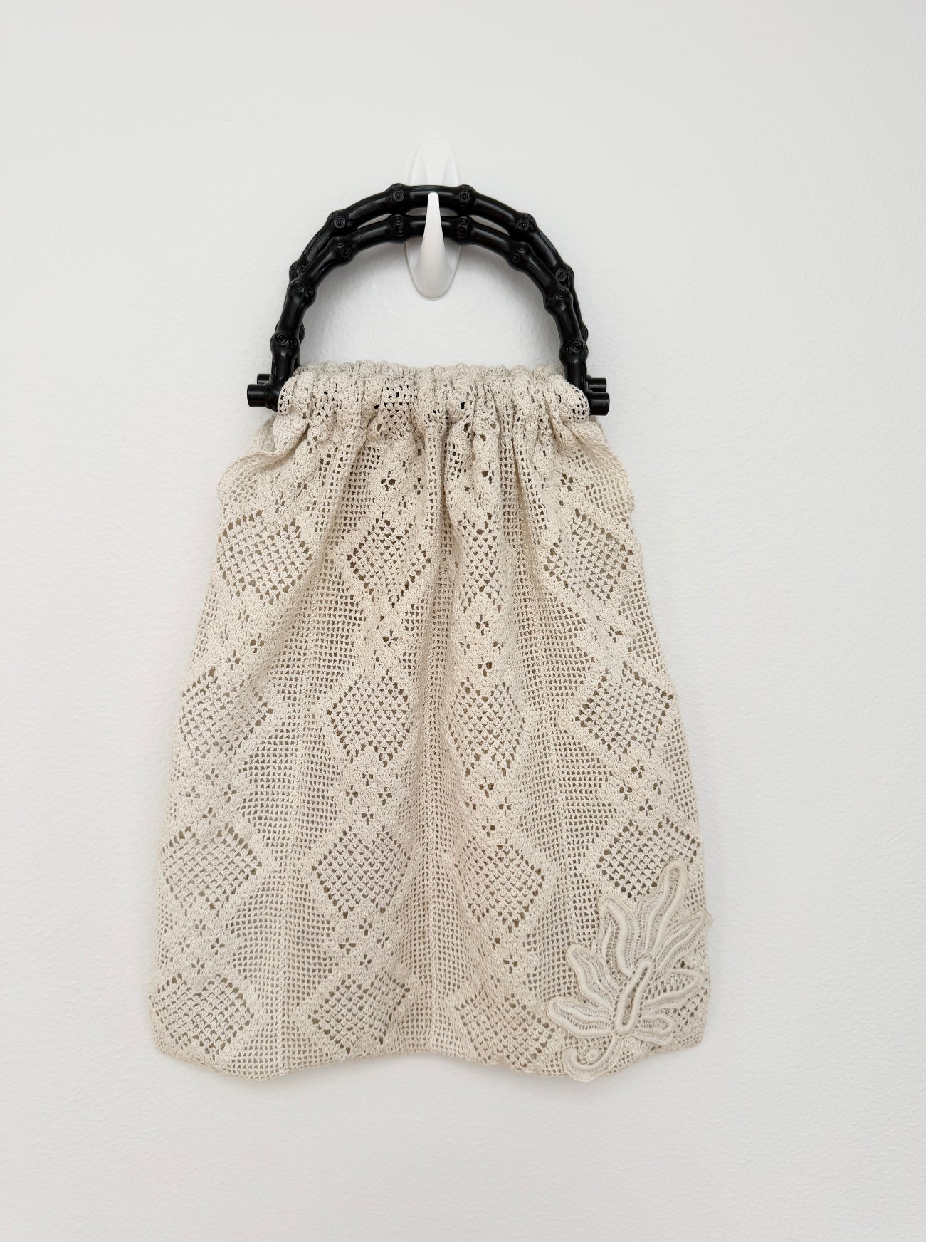 A cream-colored crochet drawstring bag with a black bamboo-style top handle, shown against a plain white background.