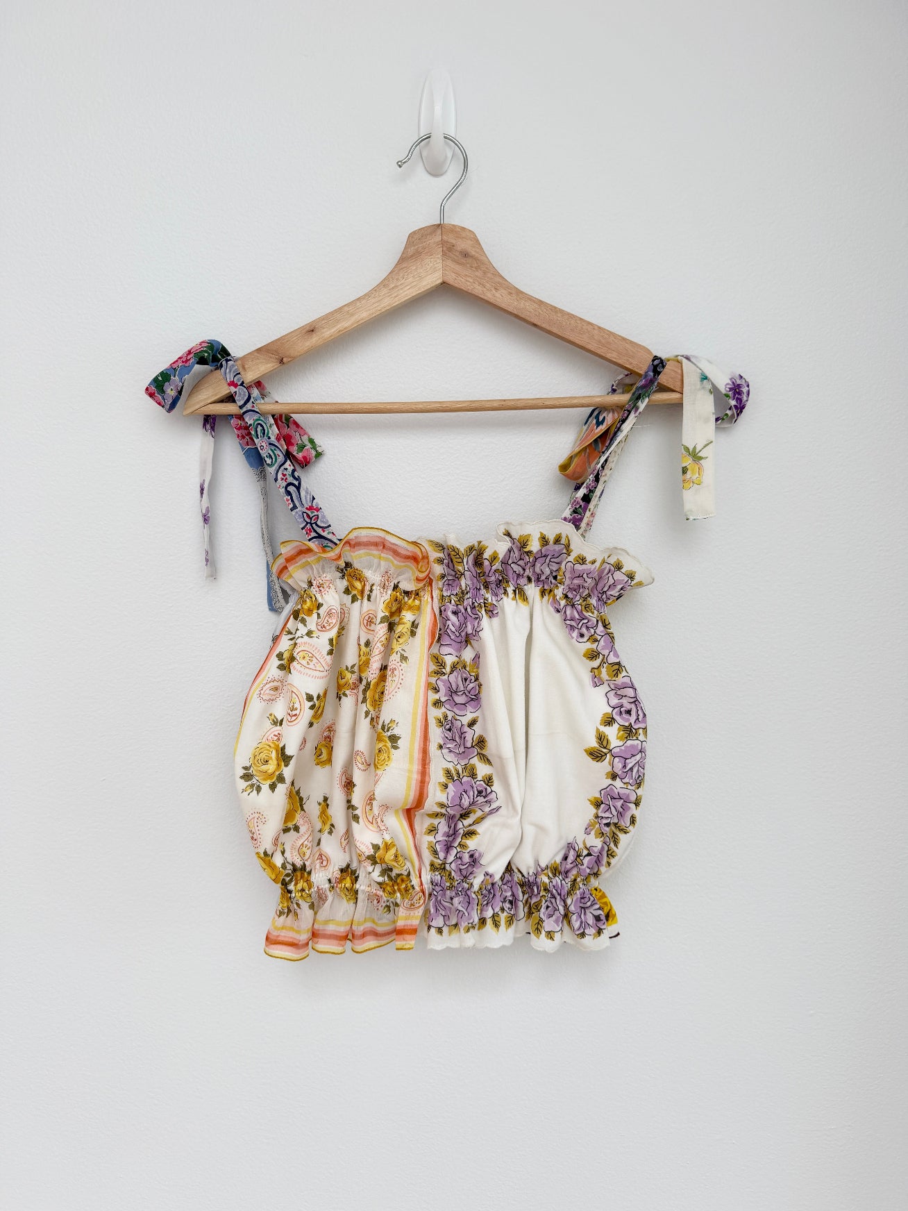 Floral top with ribbon straps on a wooden hanger against a white background