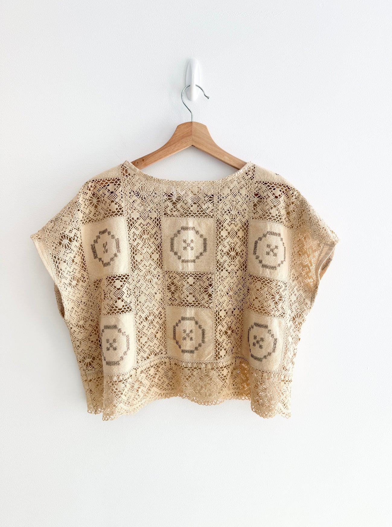 Beige crochet top with geometric pattern on a wooden hanger against a white background