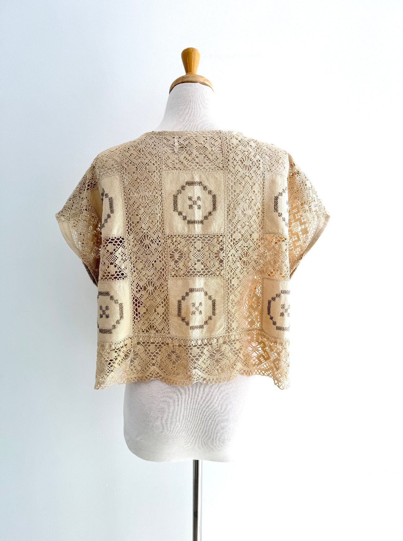 Beige knitted poncho with geometric patterns on a mannequin against a white background