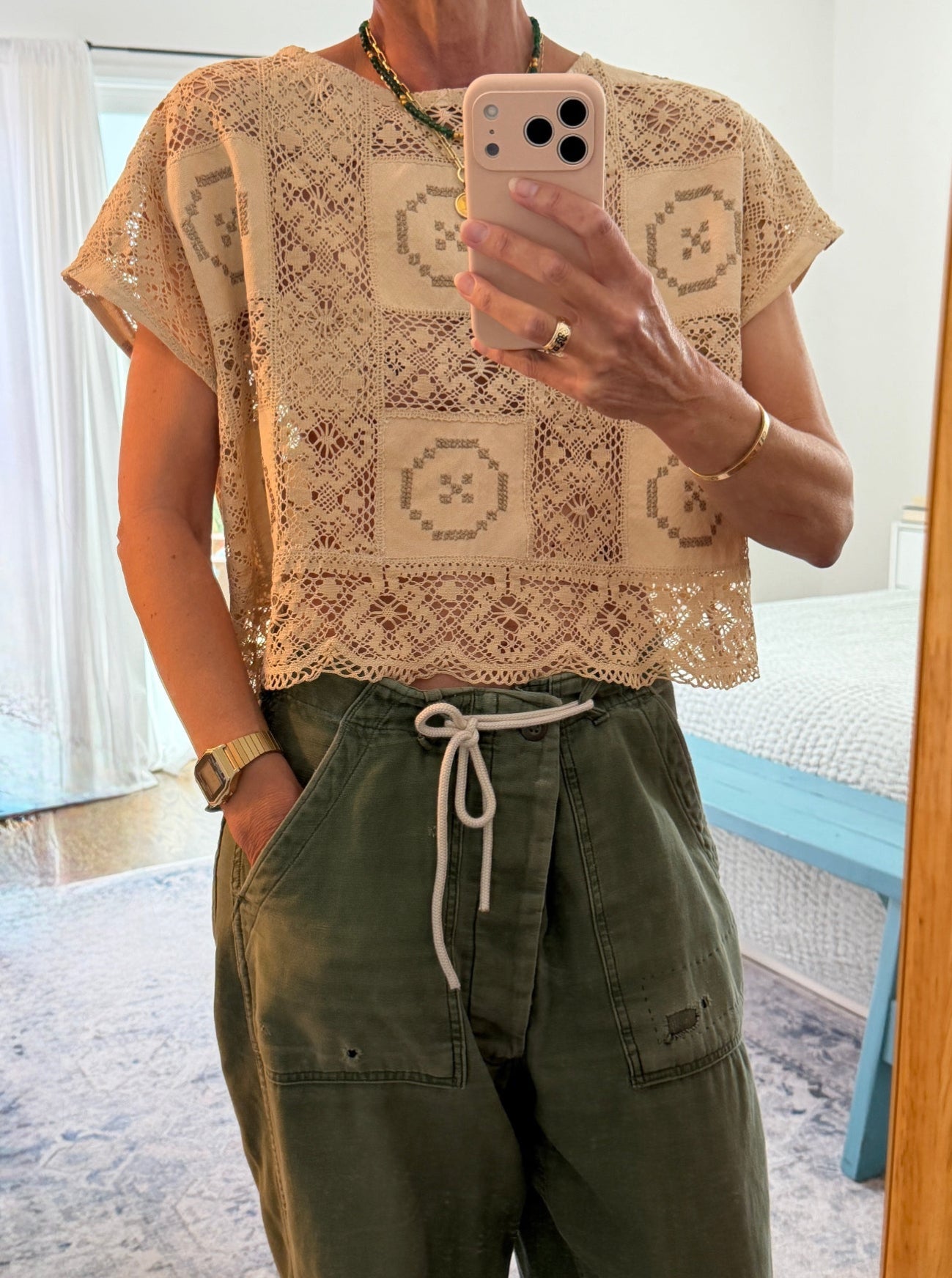 Person wearing a beige lace top and green pants, taking a mirror selfie.
