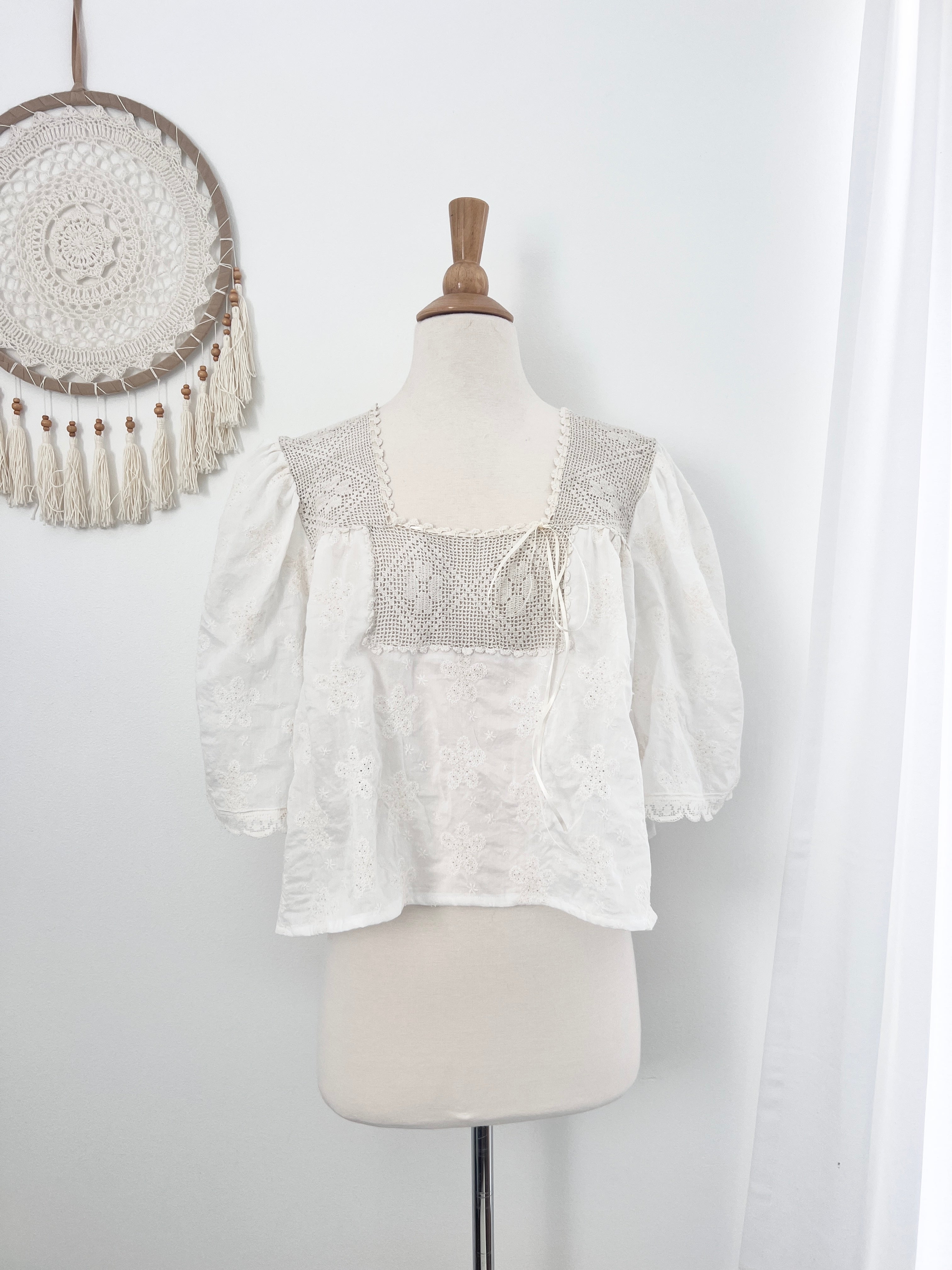 White blouse with lace detailing on a mannequin against a white background