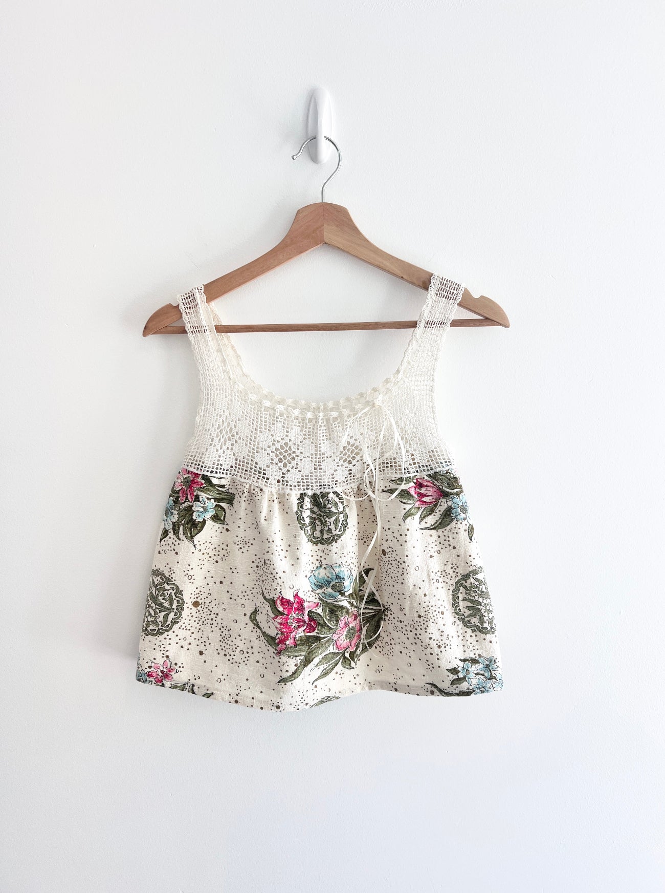 Floral print top with lace details on a wooden hanger against a white background