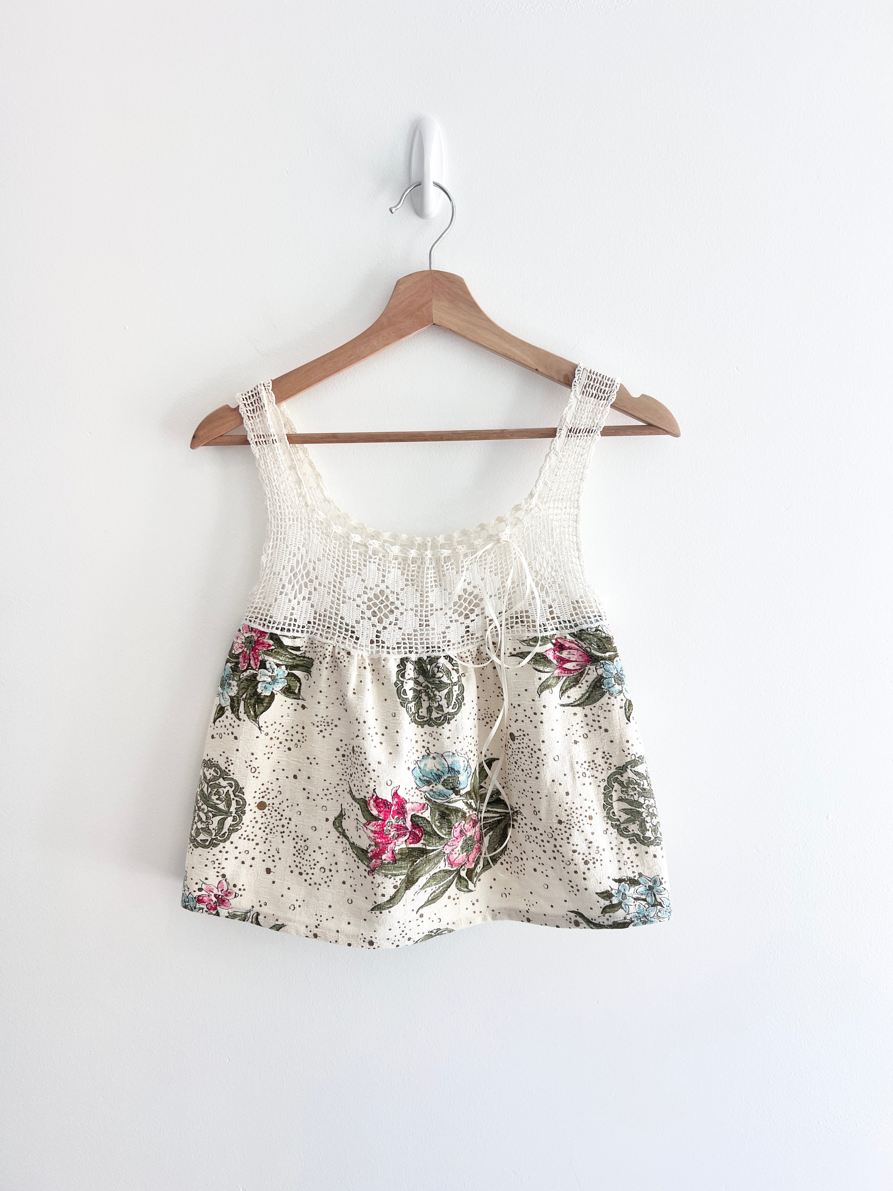 Floral print top with lace details on a wooden hanger against a white background