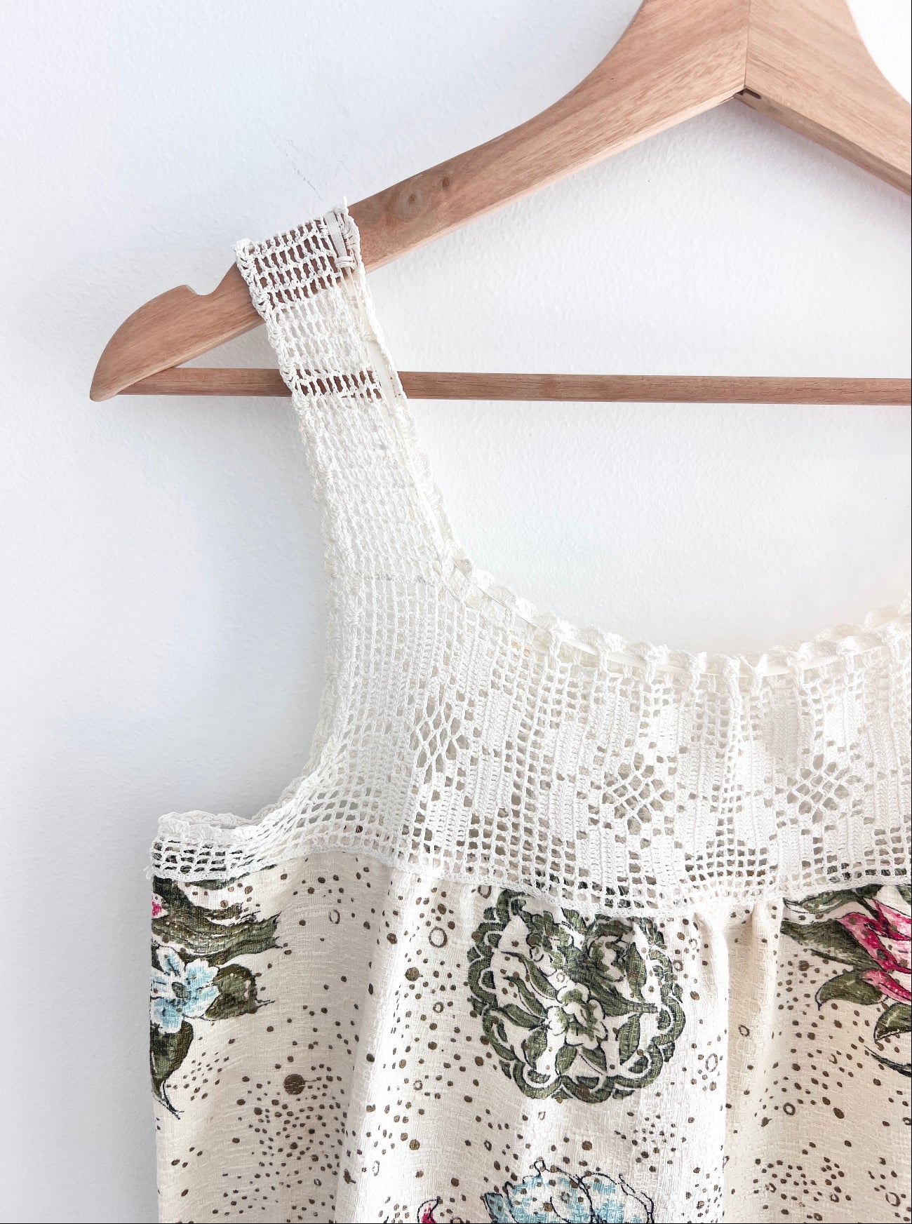 White lace top with floral patterns on a wooden hanger against a white background