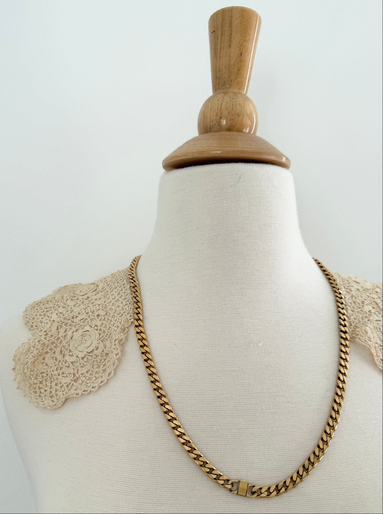 Gold chain necklace on a mannequin with a wooden base against a white background