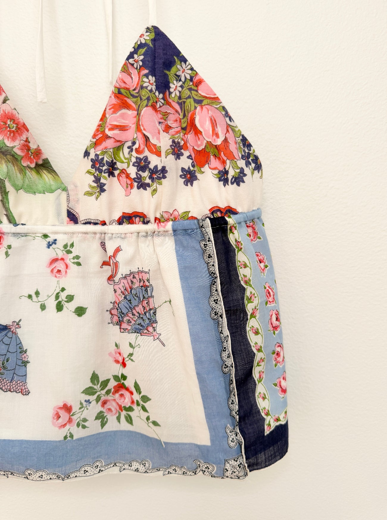 Hankie top featuring a patchwork design of floral prints, lace trim, and denim-like blue fabric panels, hanging against a plain off-white wall.