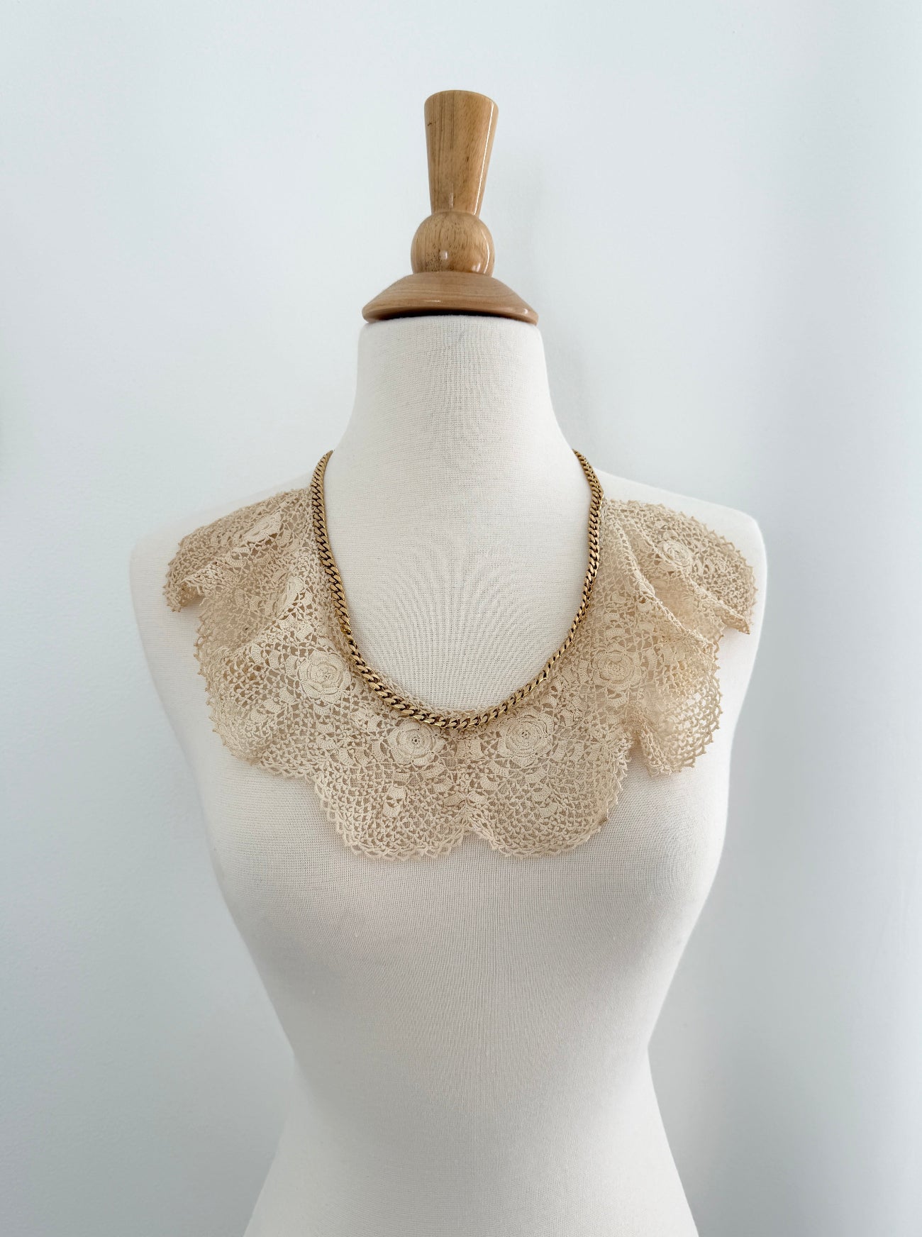 Mannequin wearing a beige lace collar and chain necklace on a white background