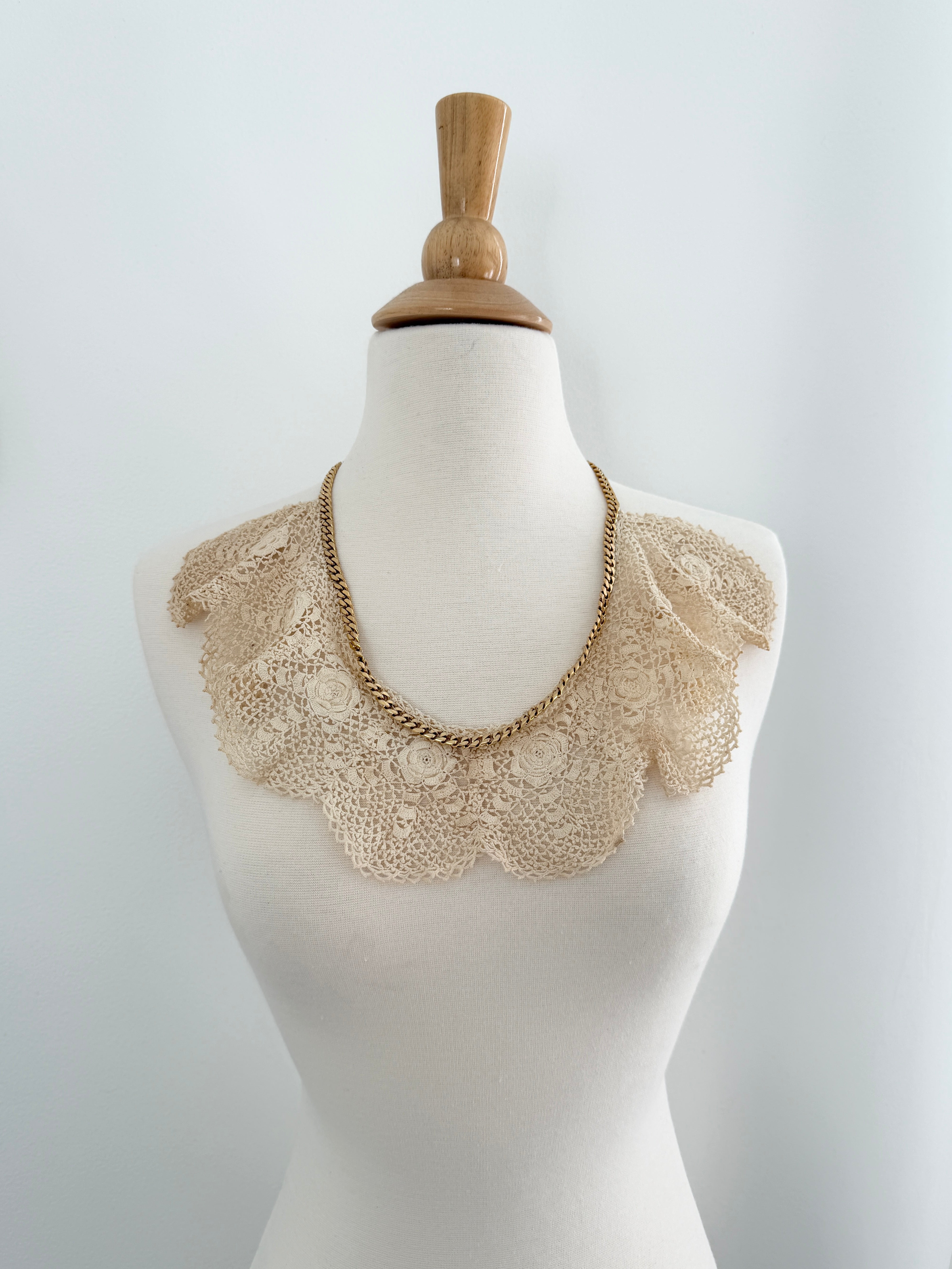 Mannequin wearing a beige lace collar and chain necklace on a white background
