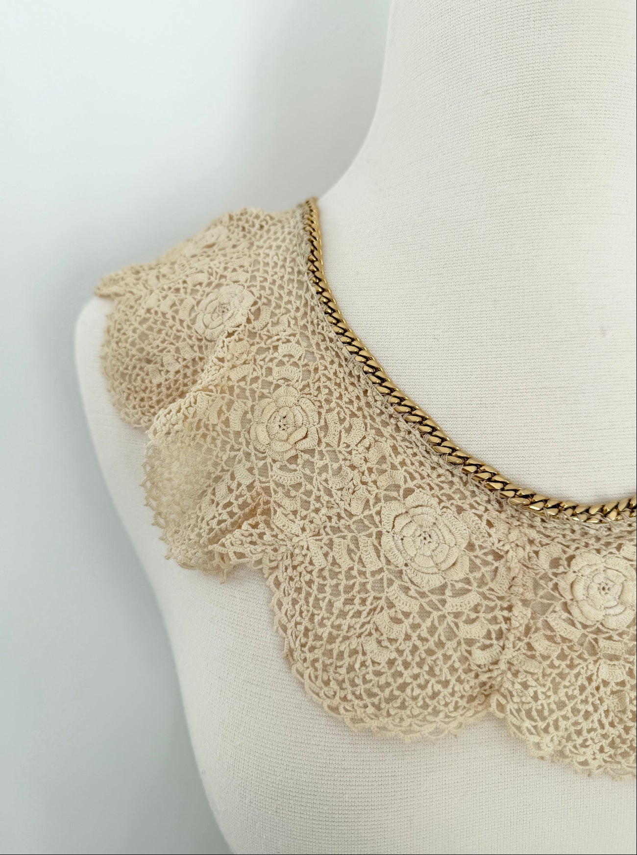 Mannequin wearing a beige lace collar with floral details on a white background