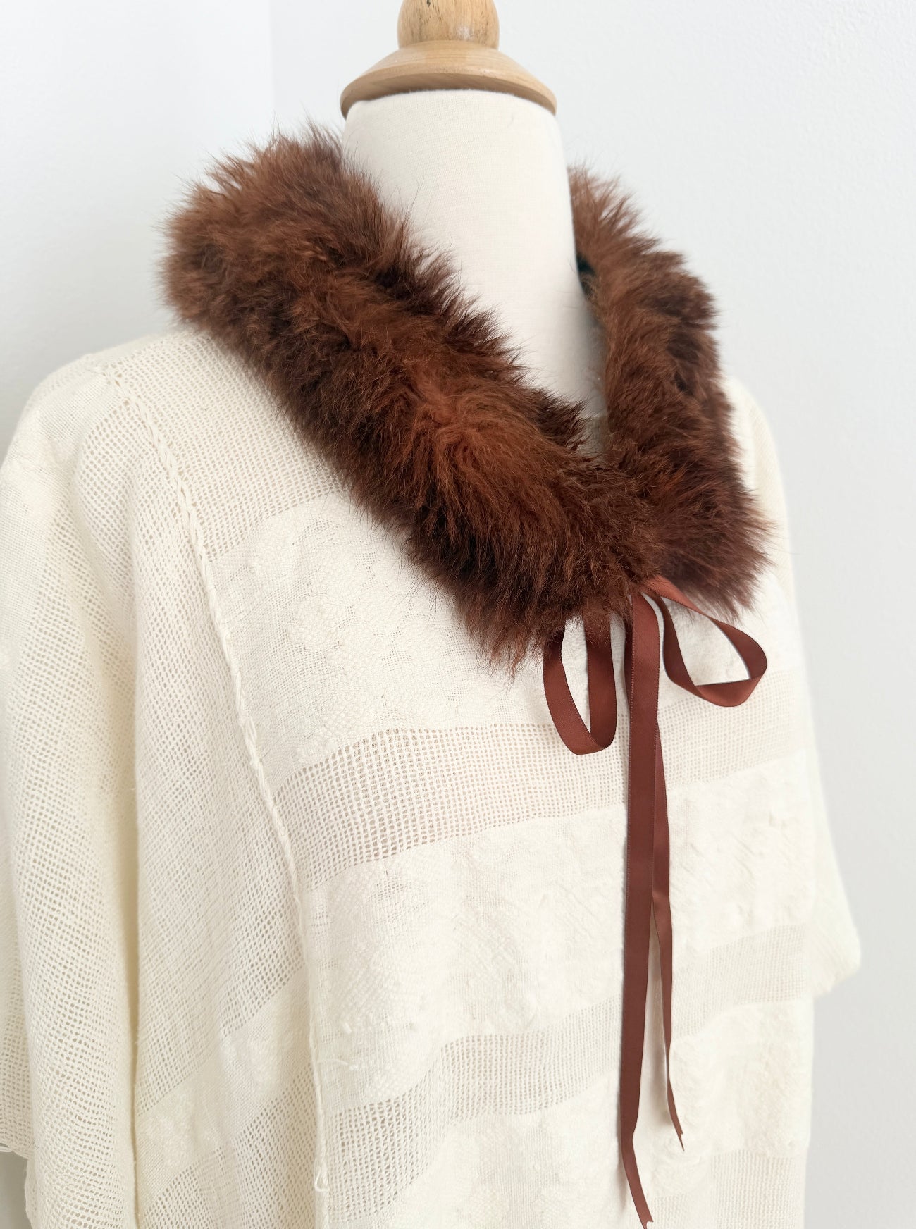 Mannequin wearing a white sweater with a brown fur collar and ribbon