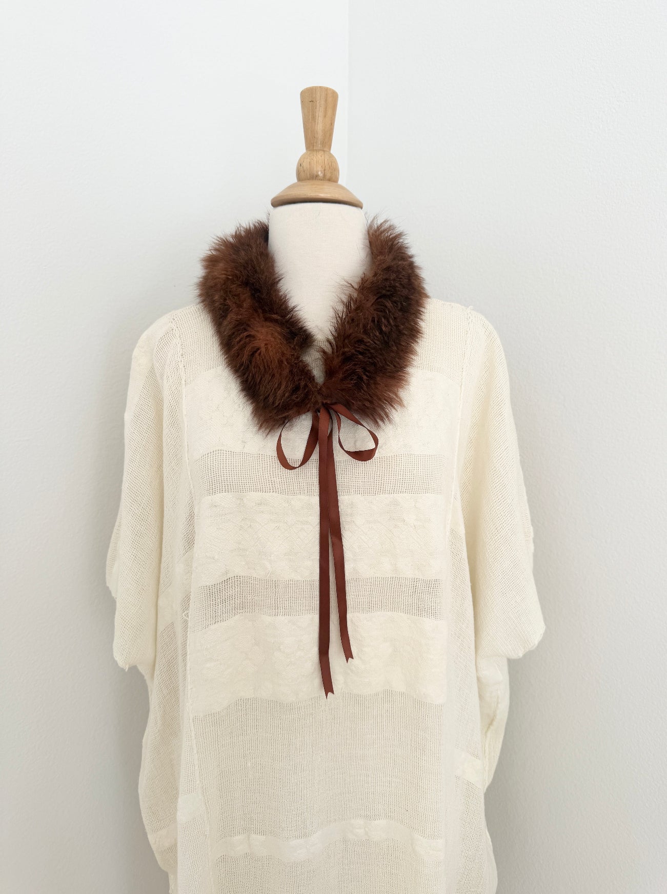 Mannequin wearing a cream-colored garment with a brown fur collar and satin tie on a white background