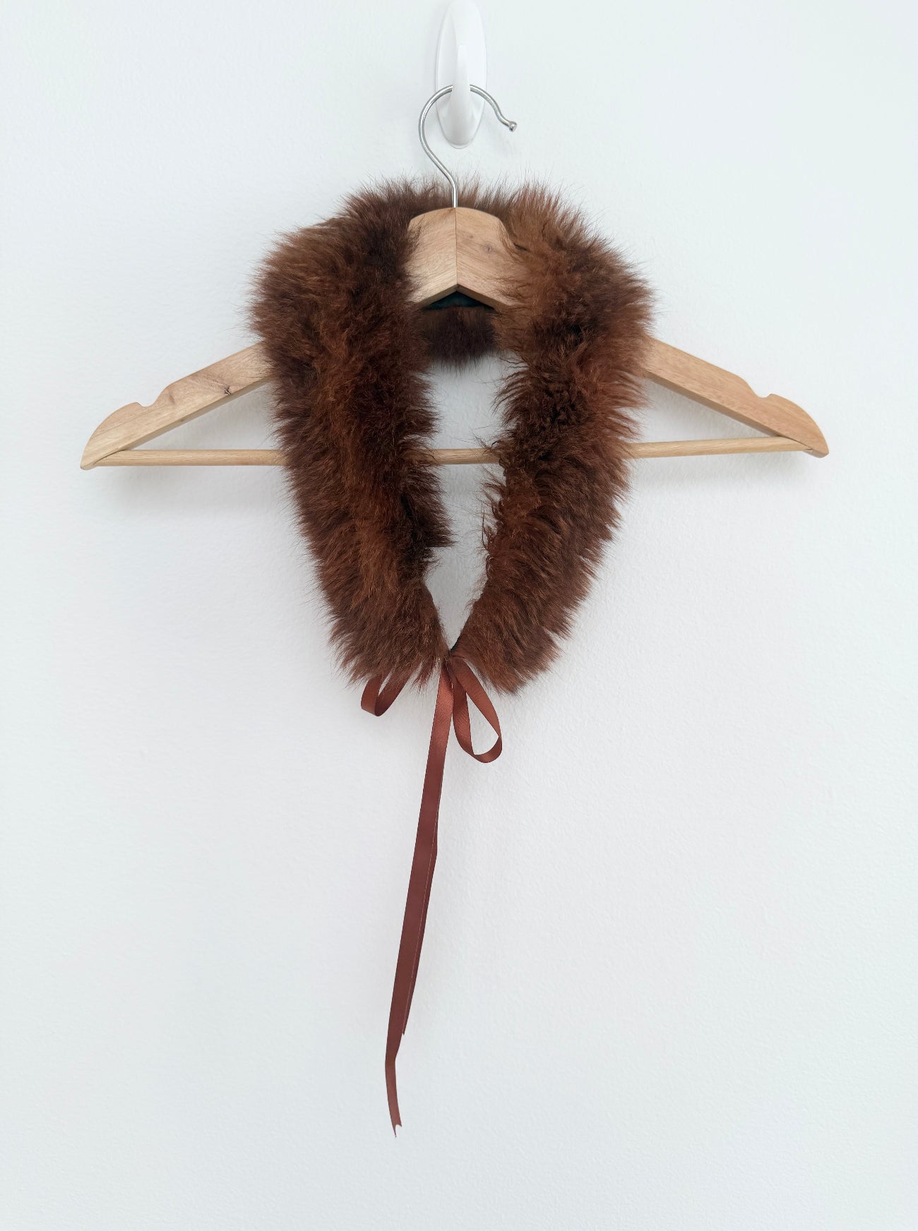 Brown fur collar with a ribbon on a wooden hanger against a white background