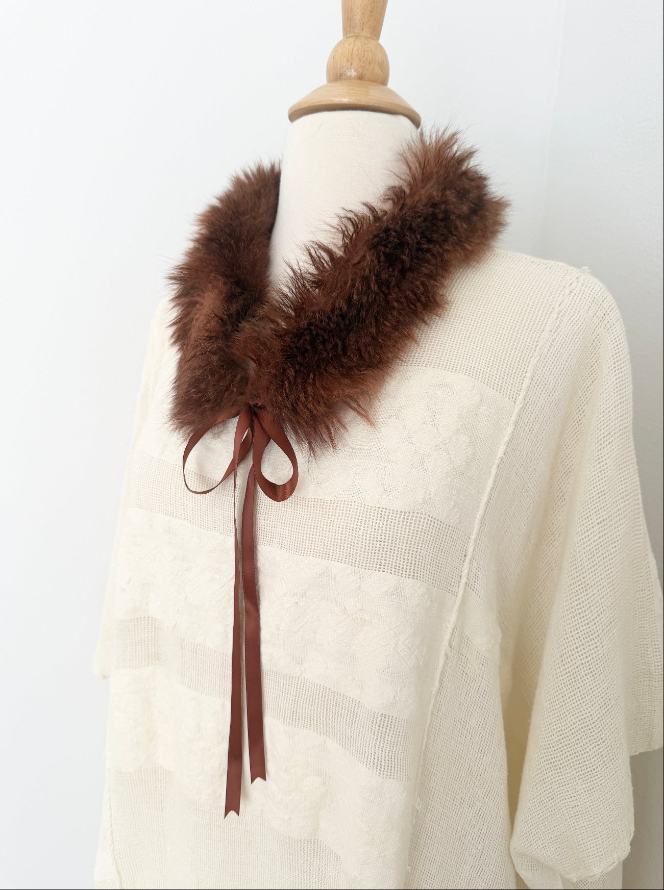 White dres with a brown fur collar and satin tie on a mannequin against a white background