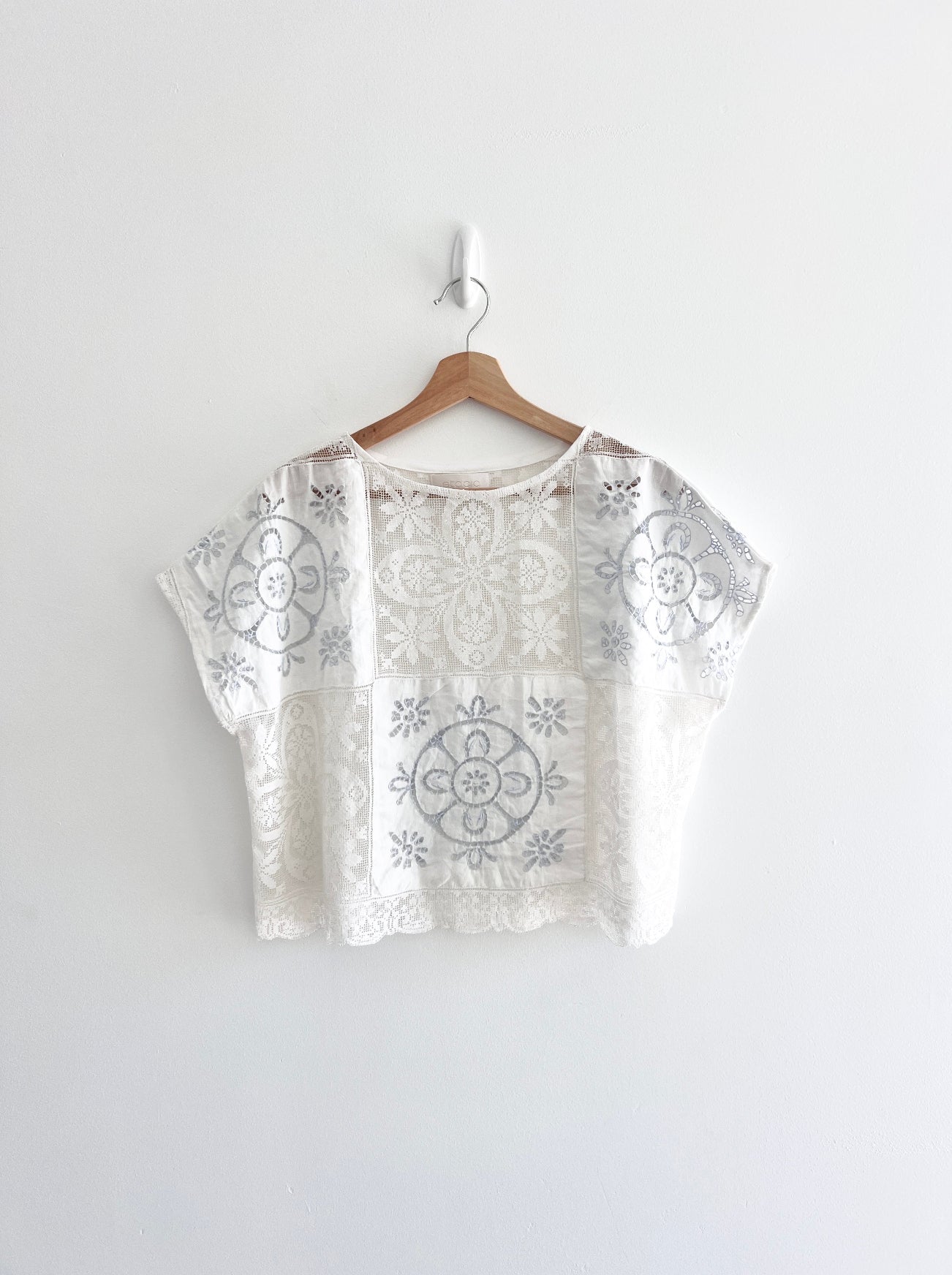 White blouse with black floral patterns on a hanger against a white background