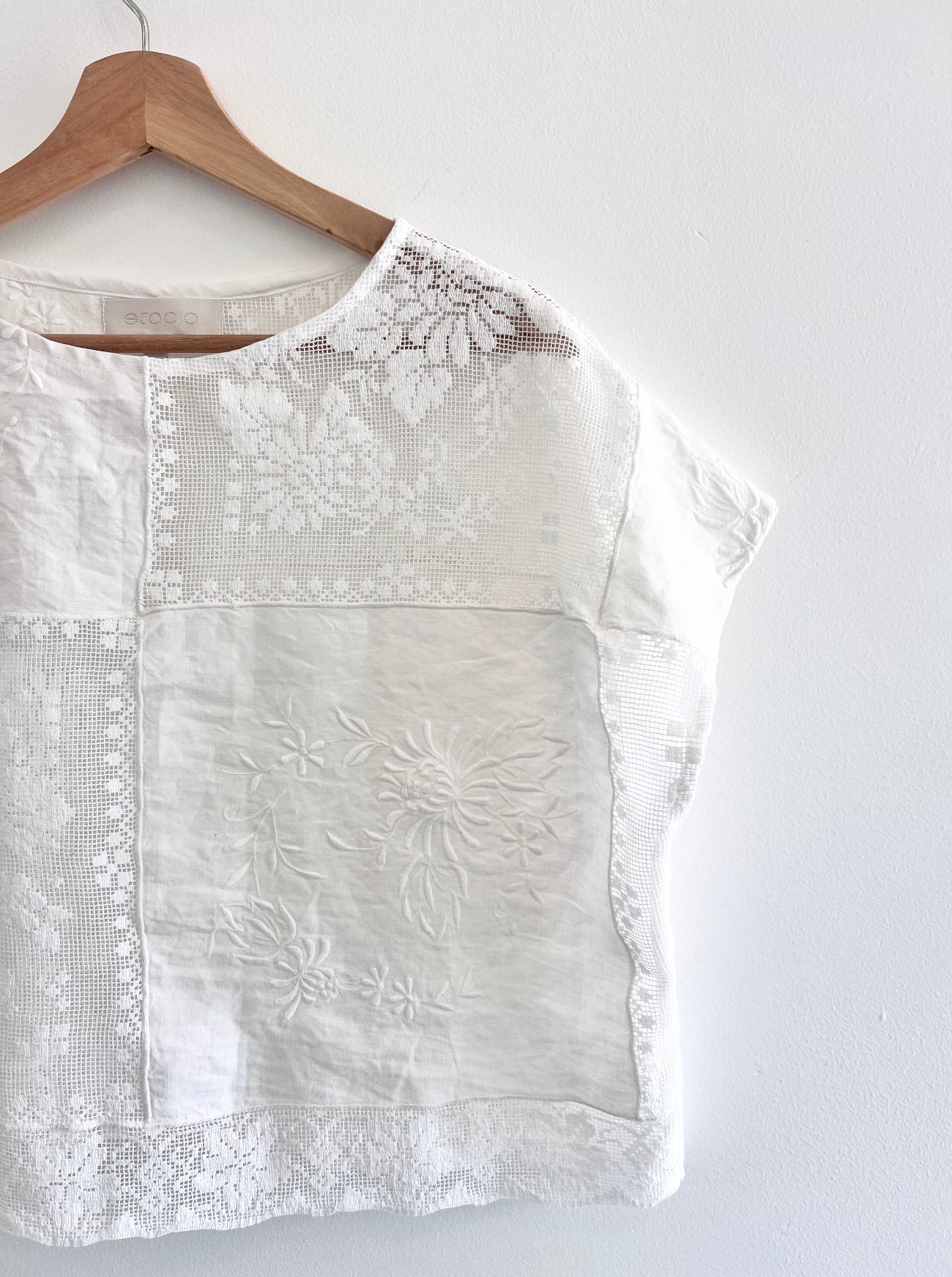 White blouse with floral embroidery on a wooden hanger against a white background
