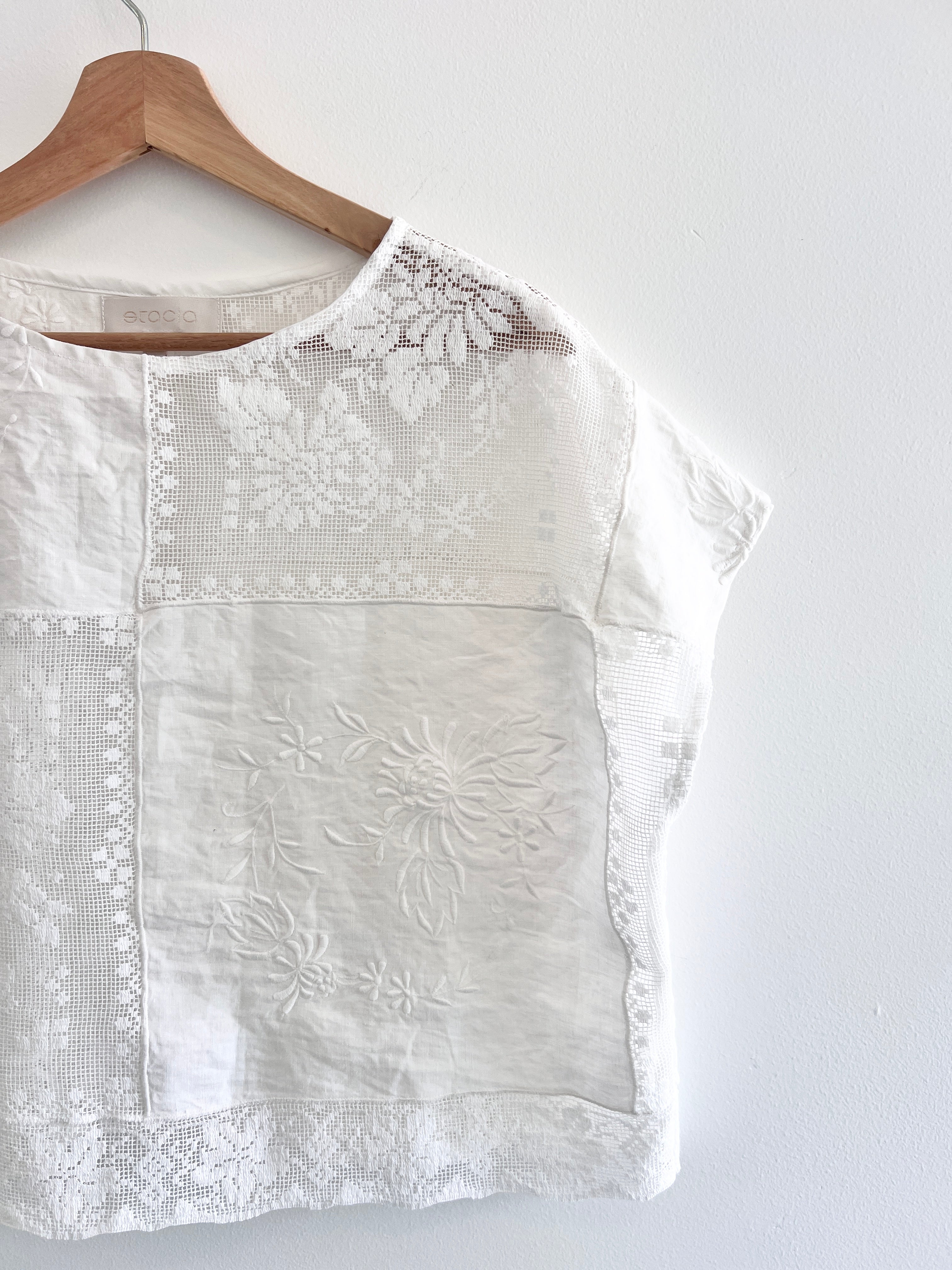 White blouse with floral embroidery on a wooden hanger against a white background