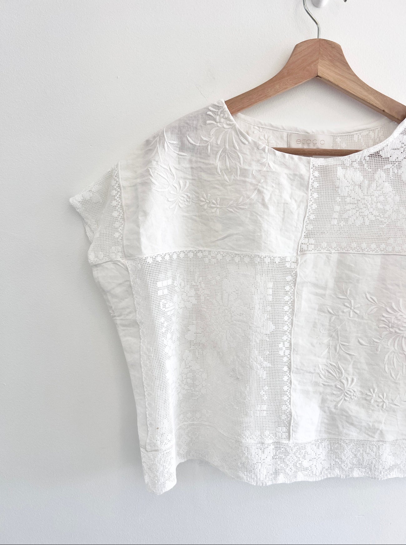 White embroidered blouse on a wooden hanger against a white background