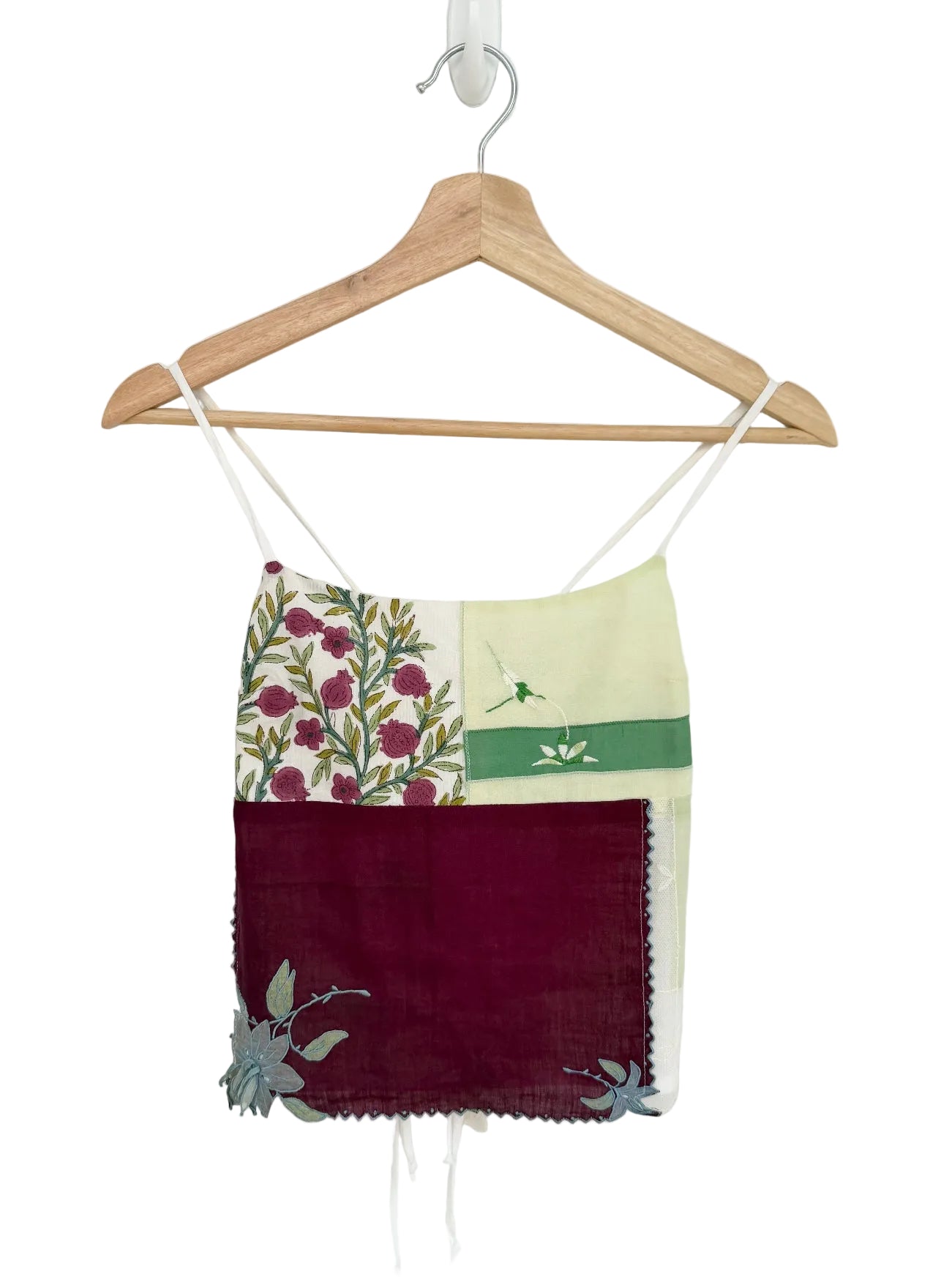 Colorful top with floral and solid patterns on a hanger against a white background