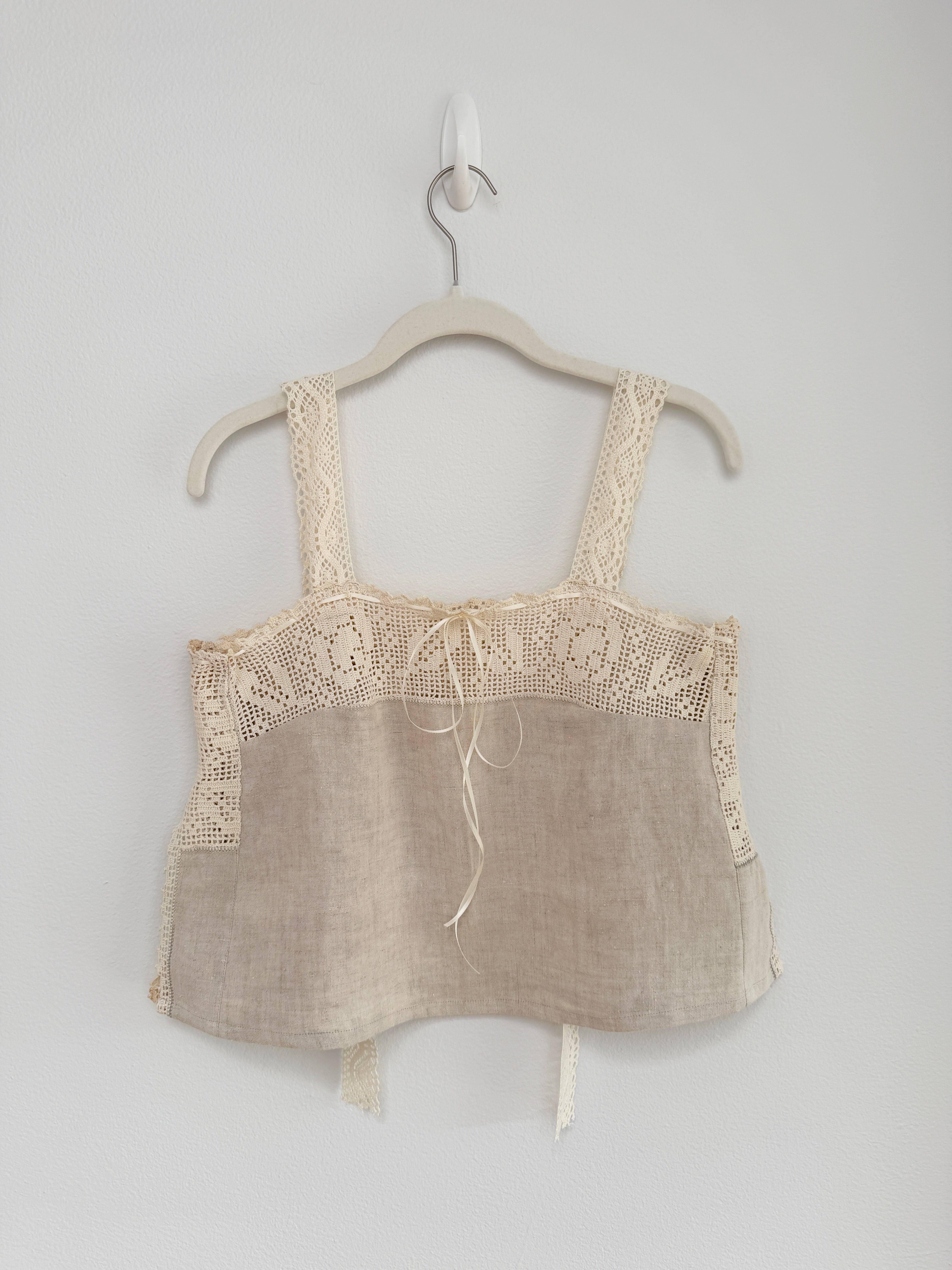 Beige lace-trimmed top on a hanger against a white background