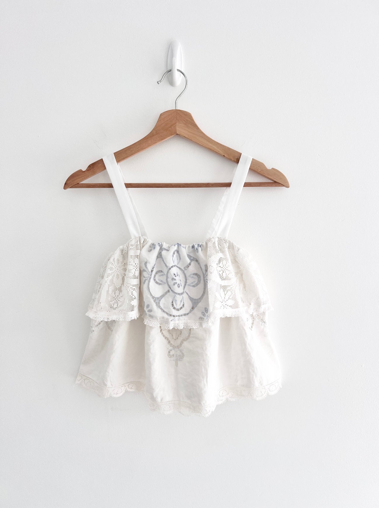 White lace top on a wooden hanger against a white background