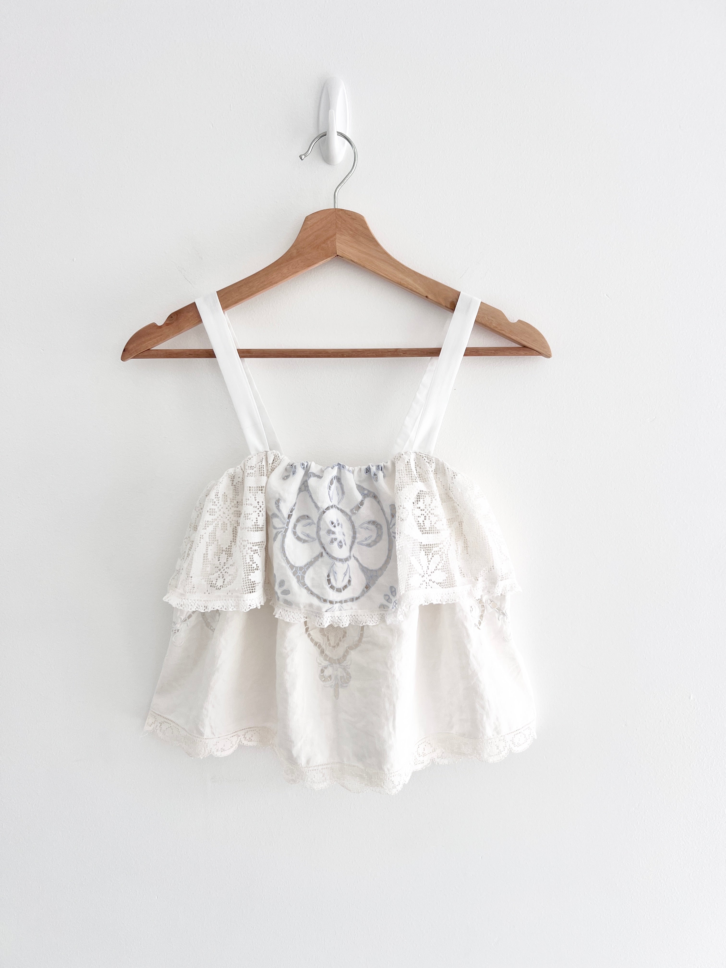 White lace top on a wooden hanger against a white background