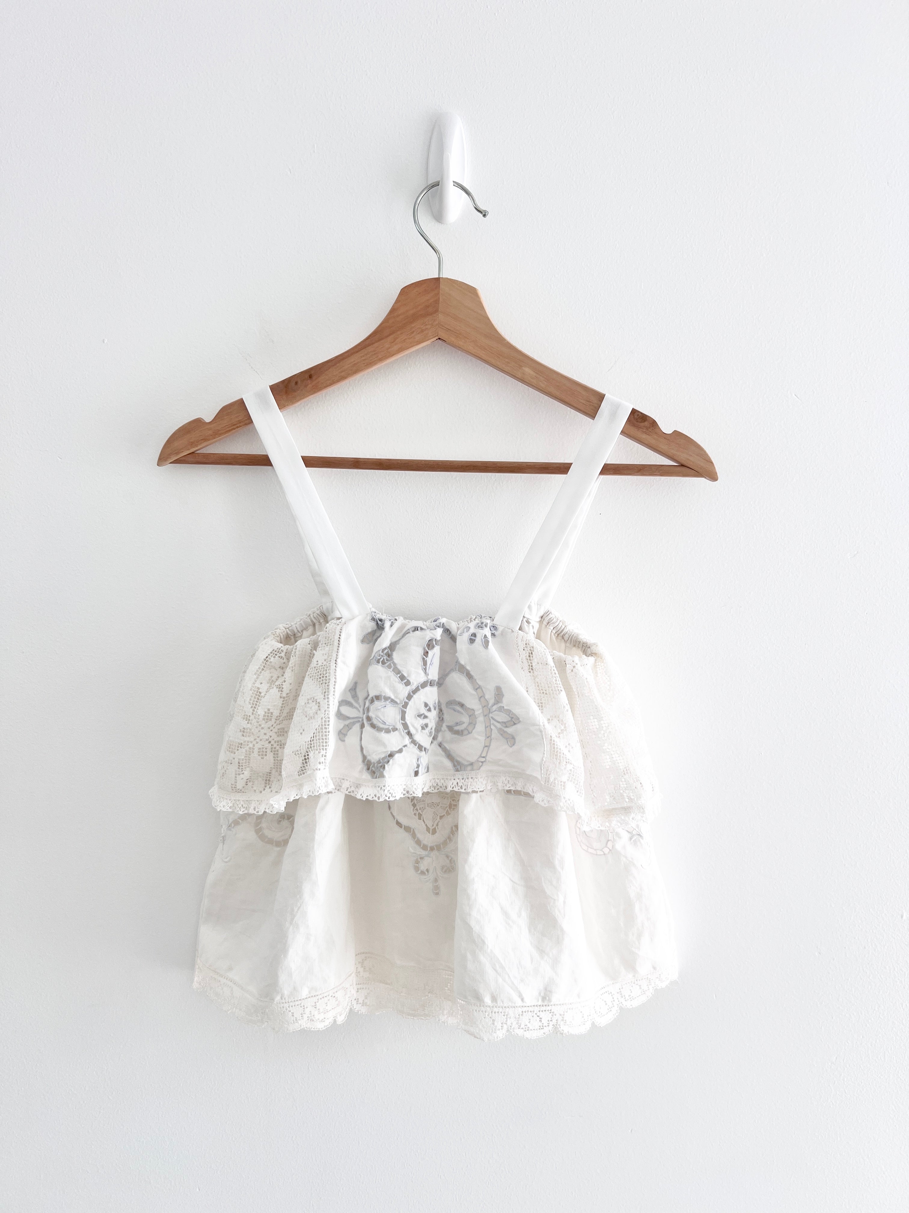 White lace top on a wooden hanger against a white background